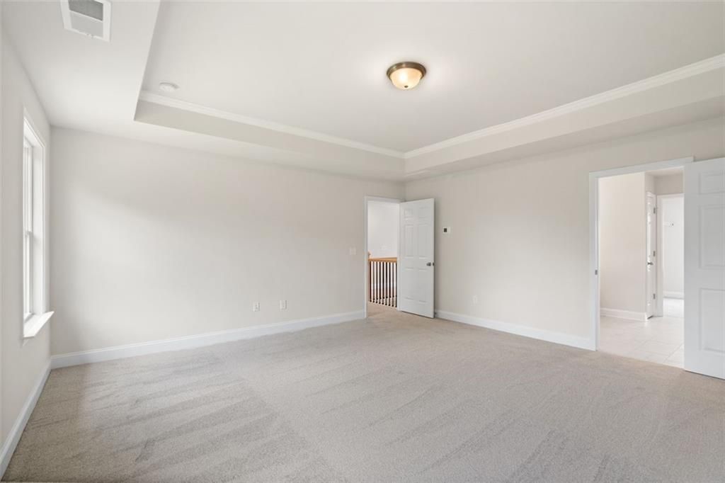 Spacious empty bedroom with tray ceiling, beige carpet, and balcony overlook in Davidson Homes The Willow D at Wehunt Meadows, Hoschton