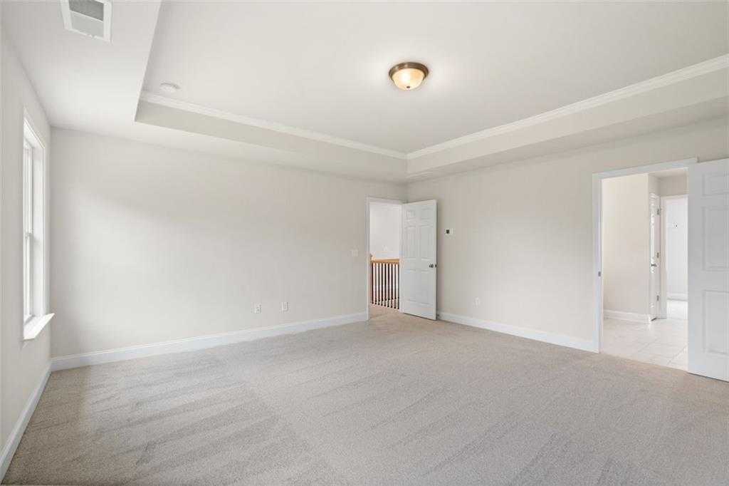 Spacious empty bedroom with tray ceiling, beige carpet, and balcony overlook in Davidson Homes The Willow D at Wehunt Meadows, Hoschton