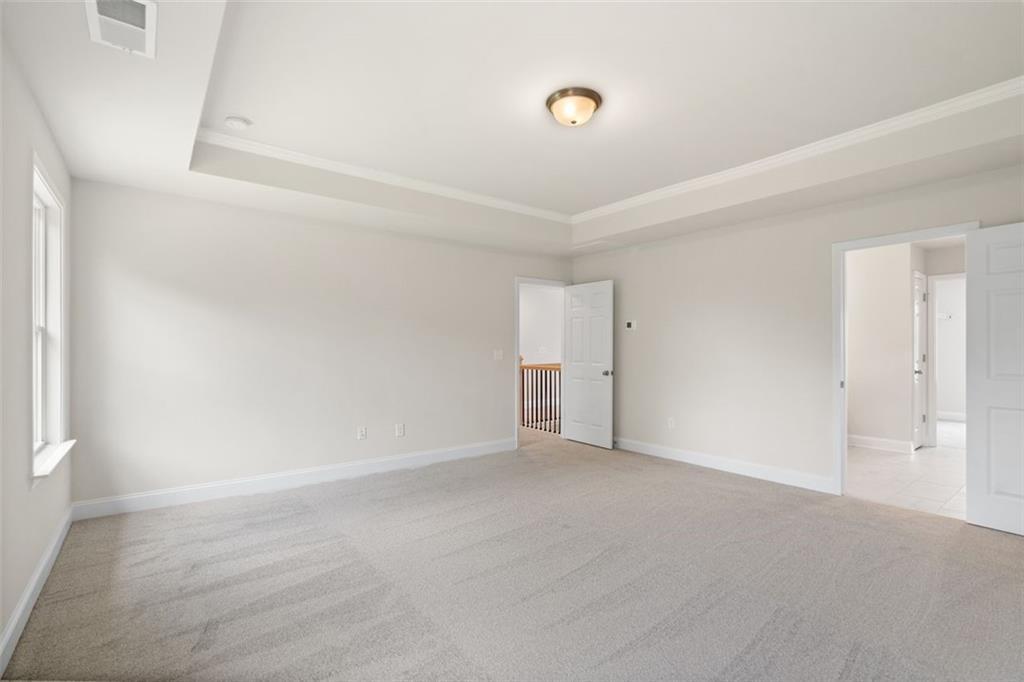 Spacious empty bedroom with tray ceiling, beige carpet, and balcony overlook in Davidson Homes The Willow D at Wehunt Meadows, Hoschton