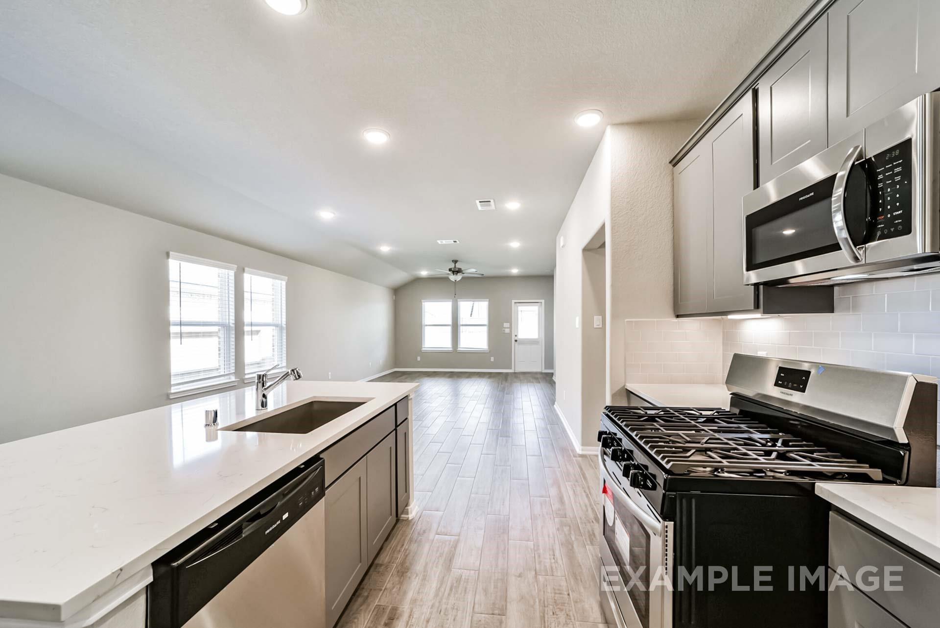 Modern open-concept kitchen with quartz countertops and stainless steel appliances in The Riviera A plan at Emberly, TX.