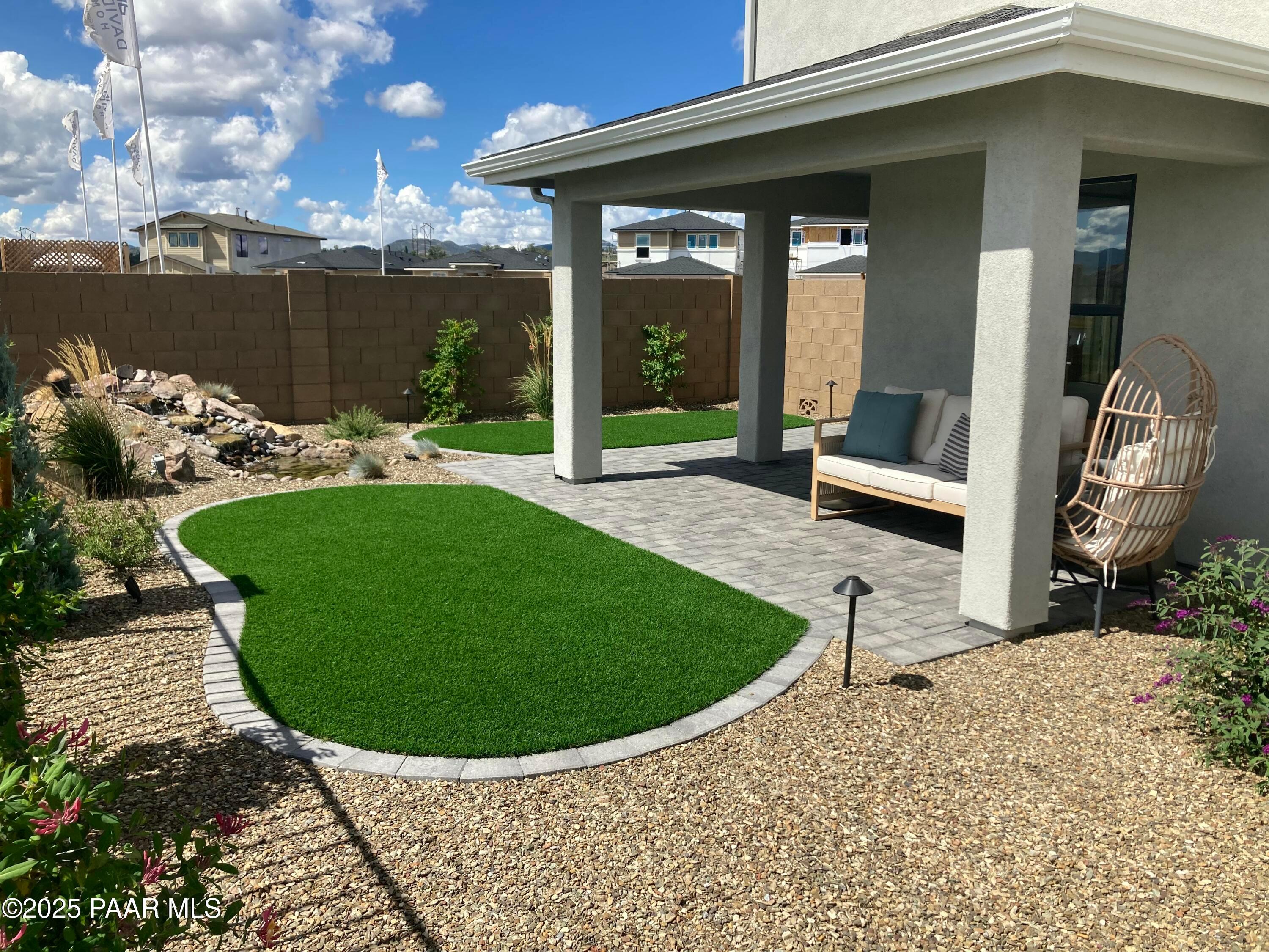 Covered patio with paver stones, artificial turf, desert gravel landscaping and hanging chair in Wilmington B home, Prescott, AZ