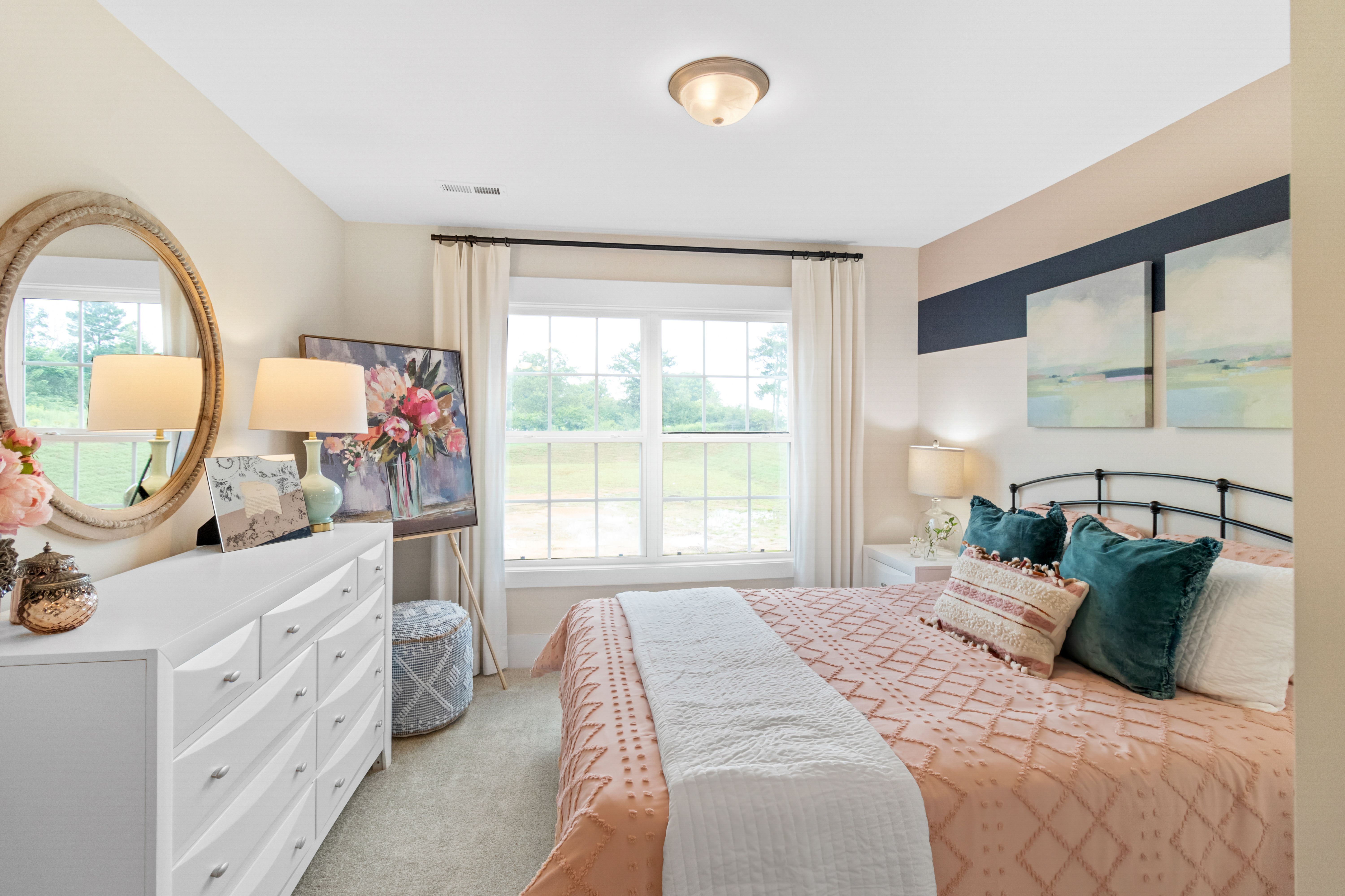 Cozy bedroom at Noble Ridge in Cullman Alabama with beige walls, tufted peach bed, white dresser, and large window view