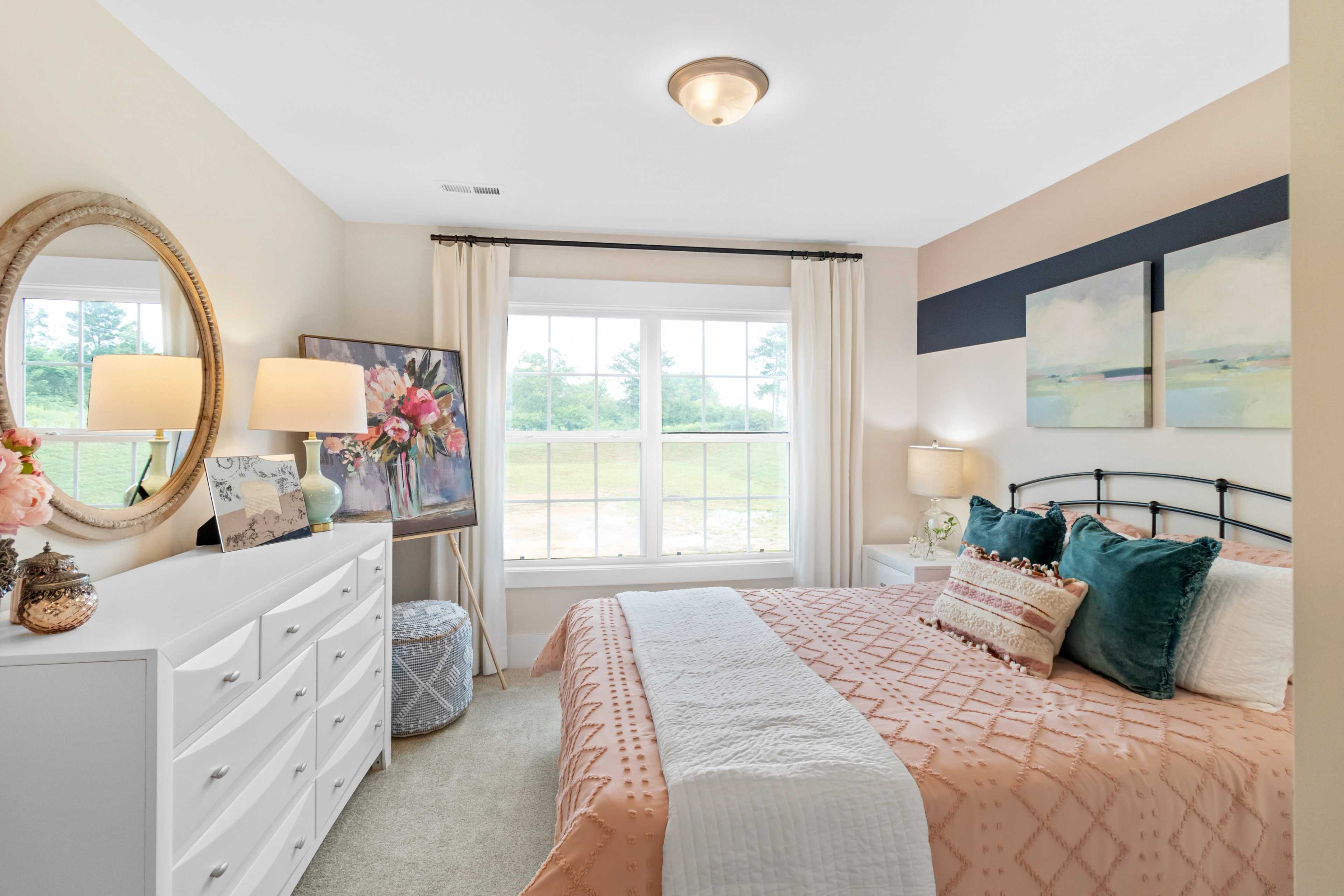 Cozy bedroom at Noble Ridge in Cullman Alabama with beige walls, tufted peach bed, white dresser, and large window view