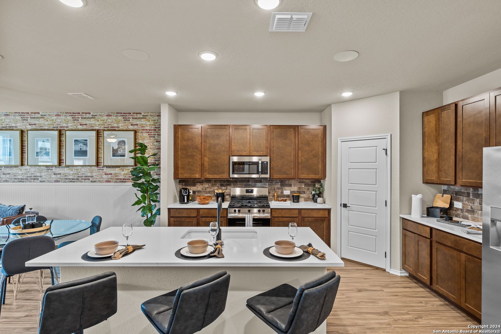 Modern kitchen with white quartz island, warm wood cabinets, stainless appliances in Davidson Homes Douglas F, Bricewood San Antonio