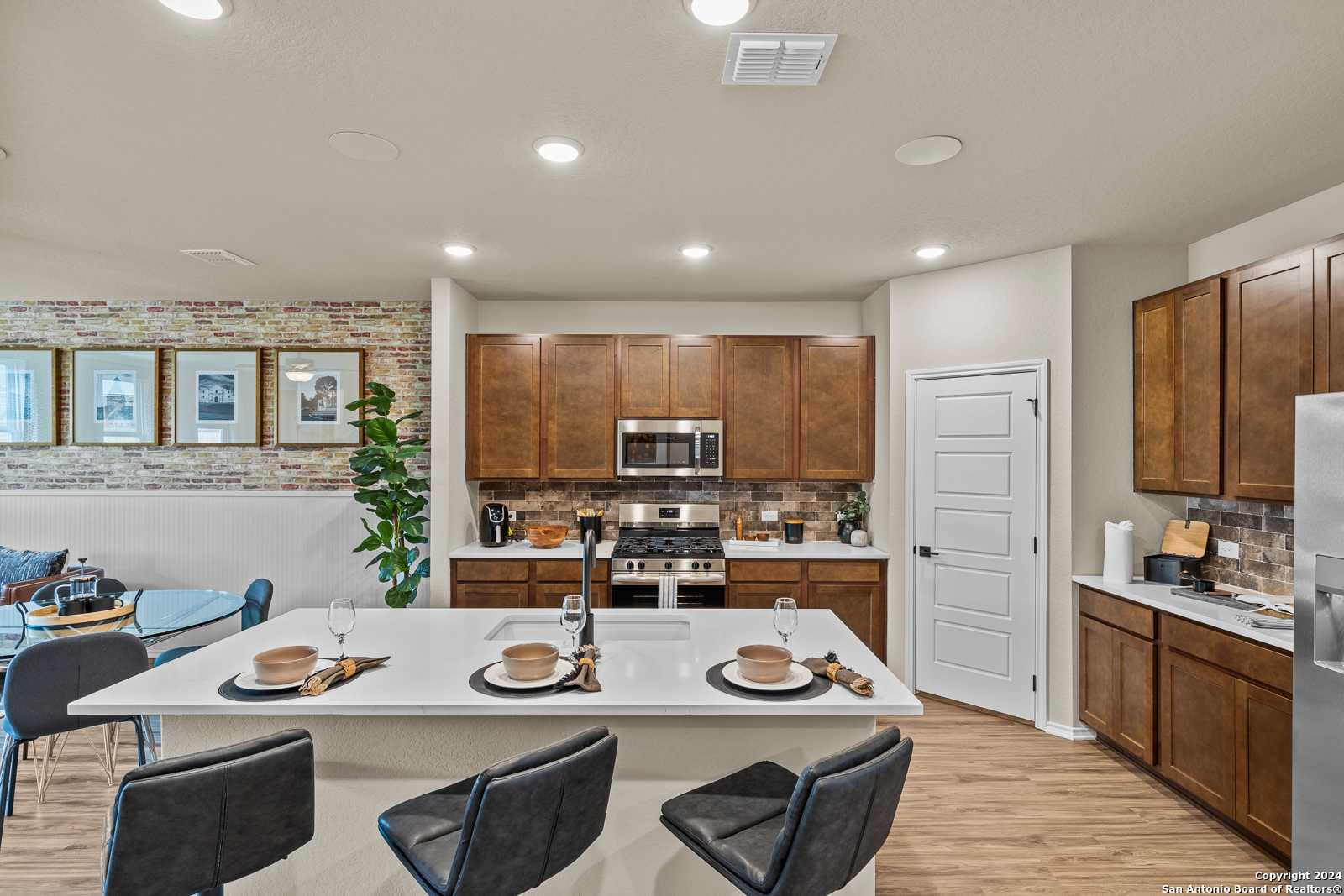 Modern kitchen with white quartz island, warm wood cabinets, stainless appliances in Davidson Homes Douglas F, Bricewood San Antonio