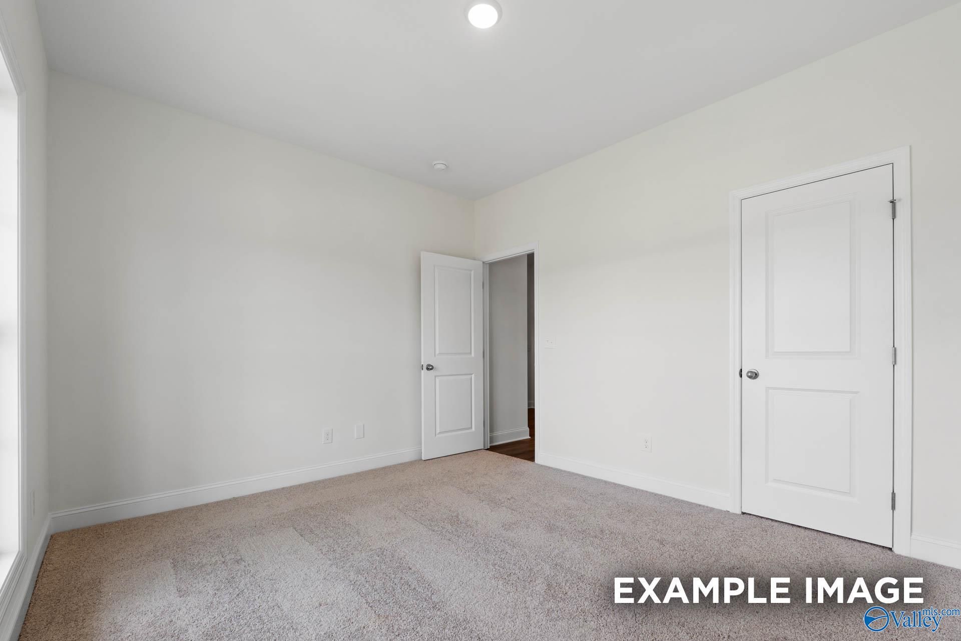 Spacious secondary bedroom with beige carpet, white walls, double doors, and window in Evermore Homes The Daphne E, Harvest AL