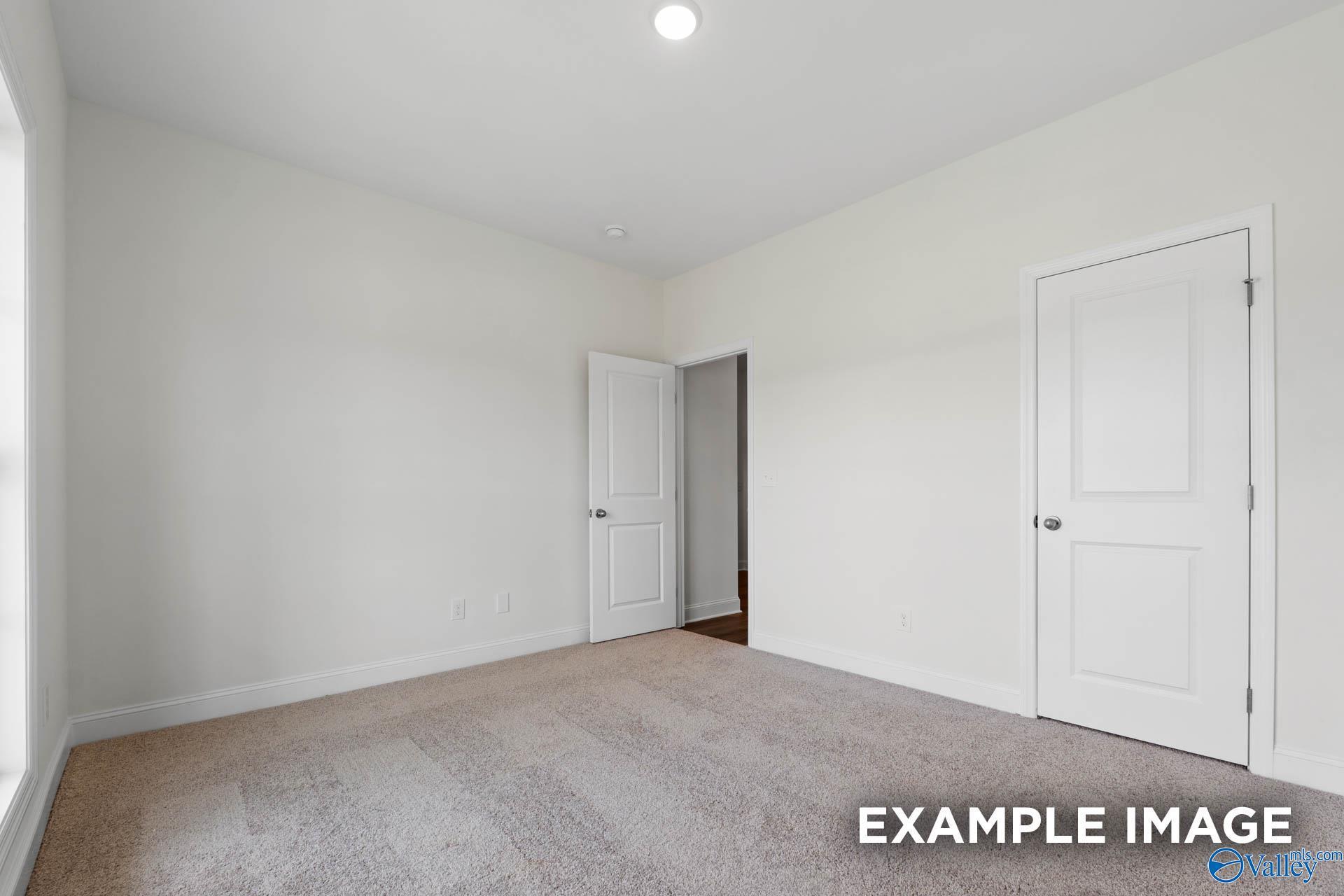 Spacious secondary bedroom with beige carpet, white walls, double doors, and window in Evermore Homes The Daphne E, Harvest AL