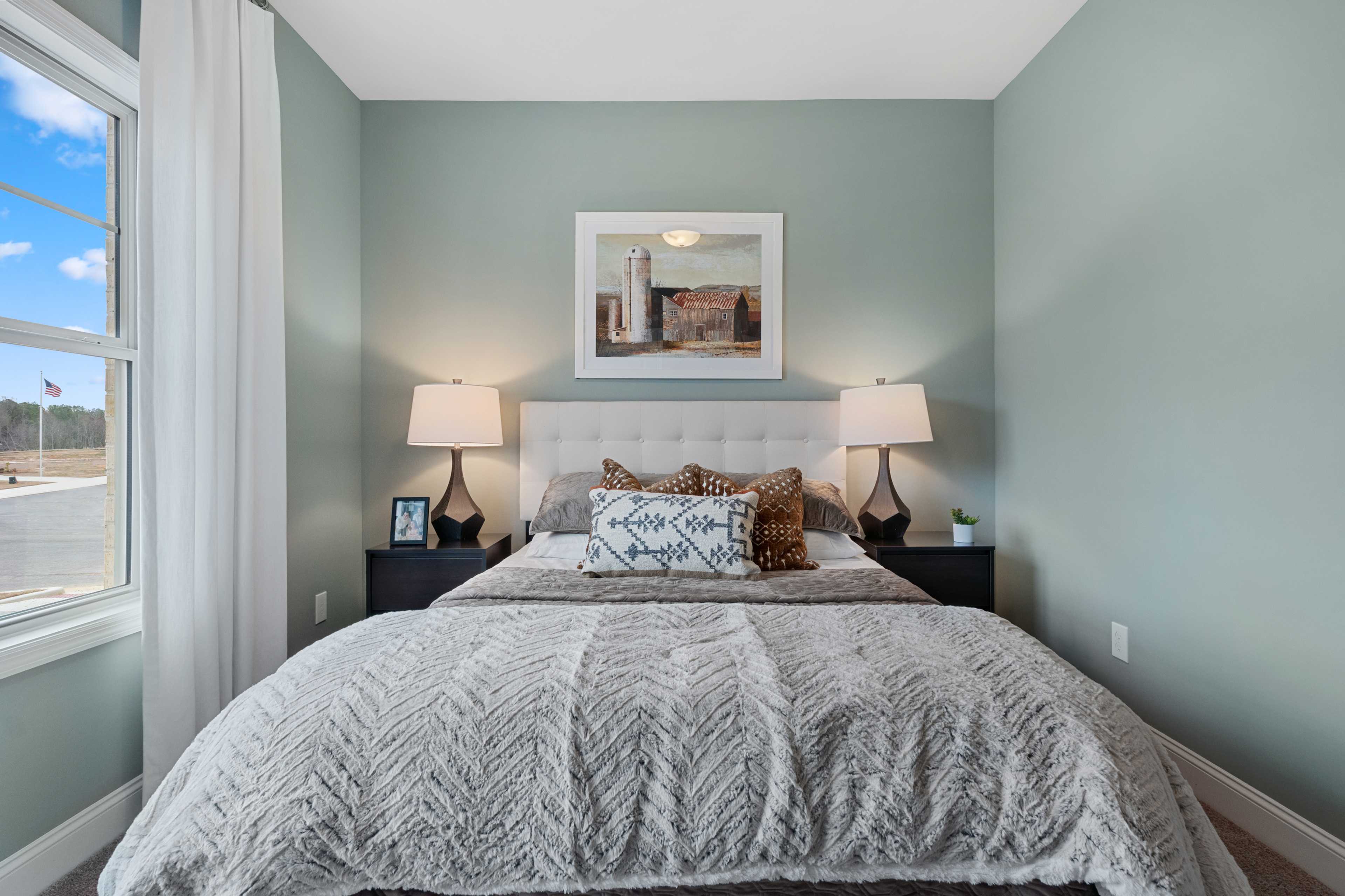 Serene sage green bedroom at The Retreat at Cain Park in Hartselle Alabama with white upholstered bed gray duvet and barn artwork