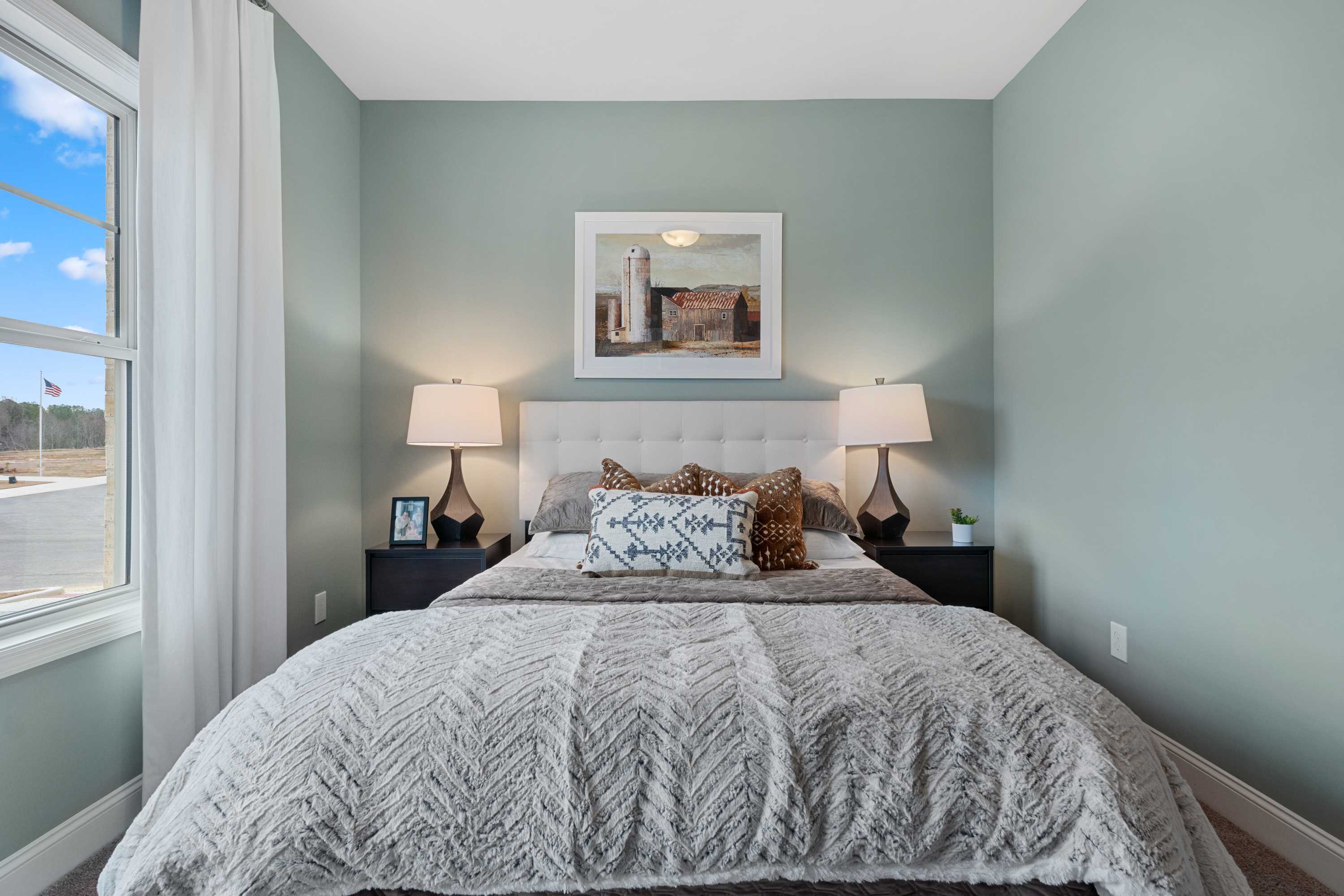 Serene sage green bedroom at The Retreat at Cain Park in Hartselle Alabama with white upholstered bed gray duvet and barn artwork