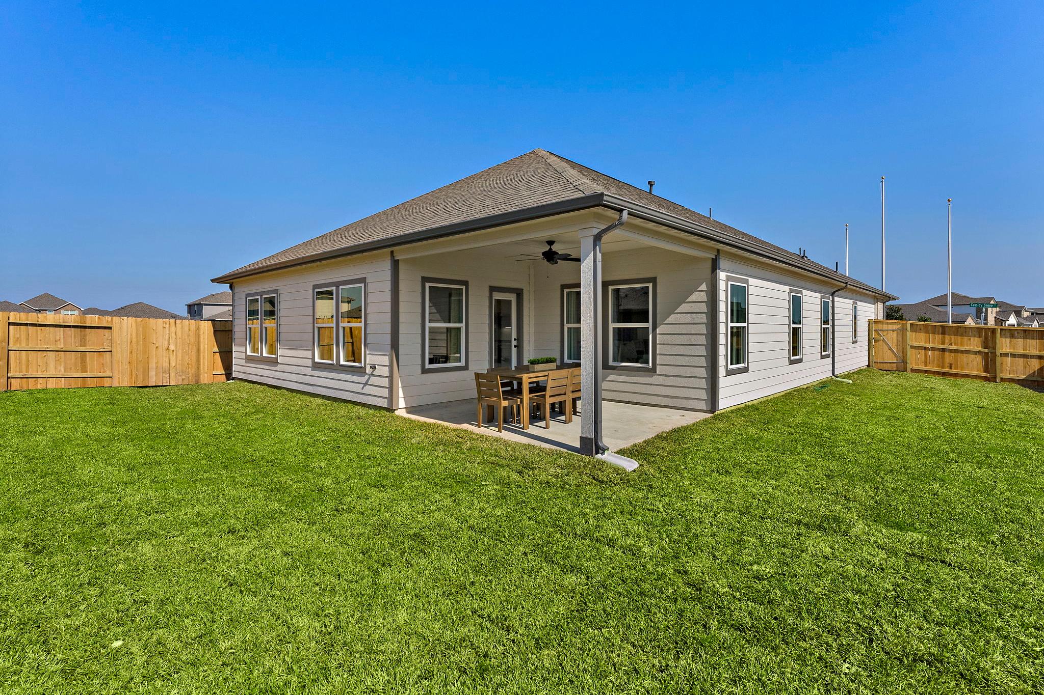 Modern single-story home exterior at Sundance Cove in Crosby Texas with covered patio, ceiling fan, outdoor dining set, and fenced green yard