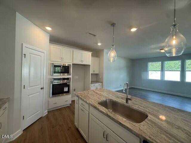 Modern open-concept kitchen with white cabinets, granite countertops, stainless oven, and pendant lights in Davidson Homes Preston C, Lillington, NC
