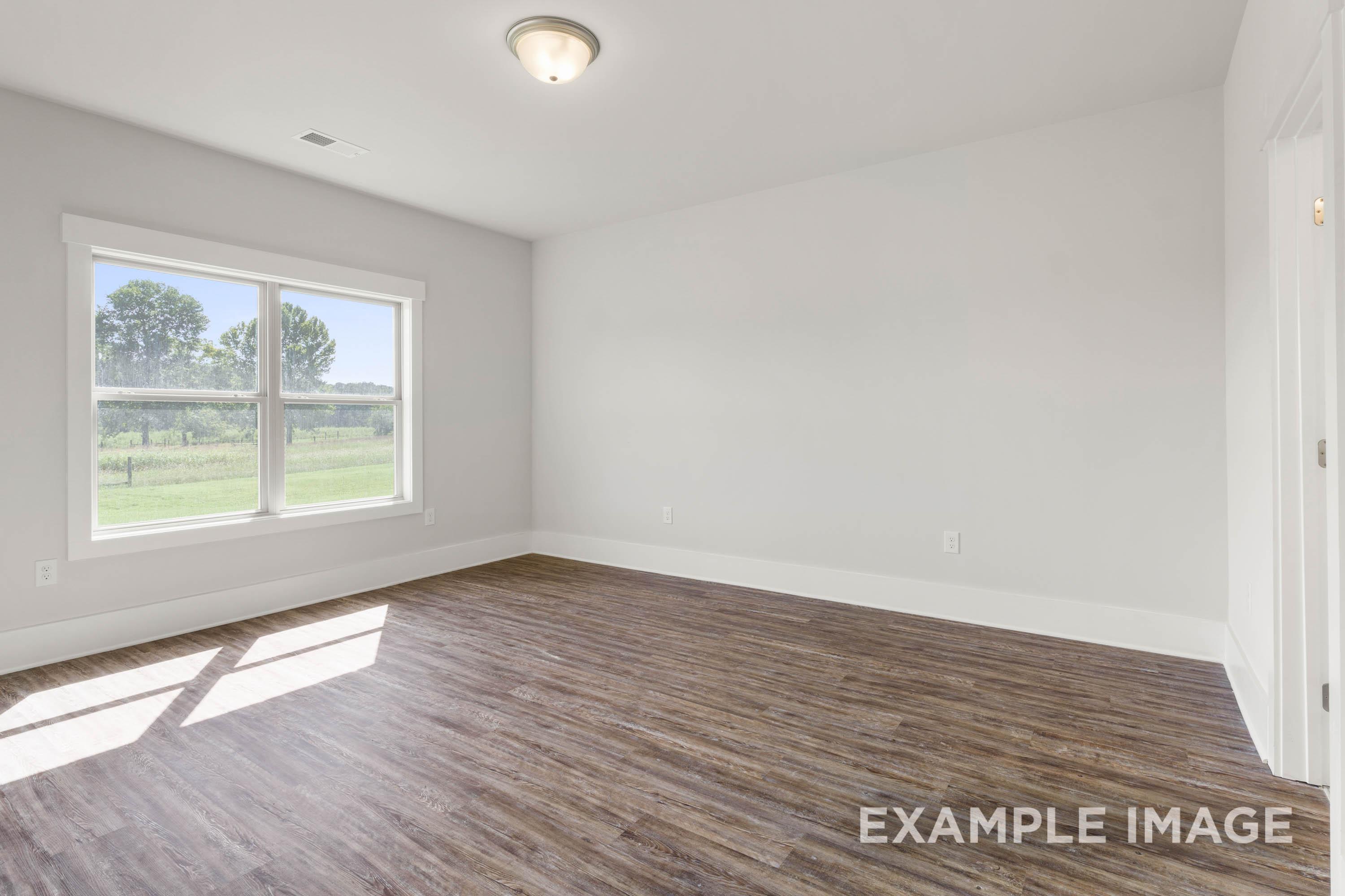 Spacious bedroom in The Richmond D featuring wood-style flooring, neutral walls, and natural light in New Market, Alabama.