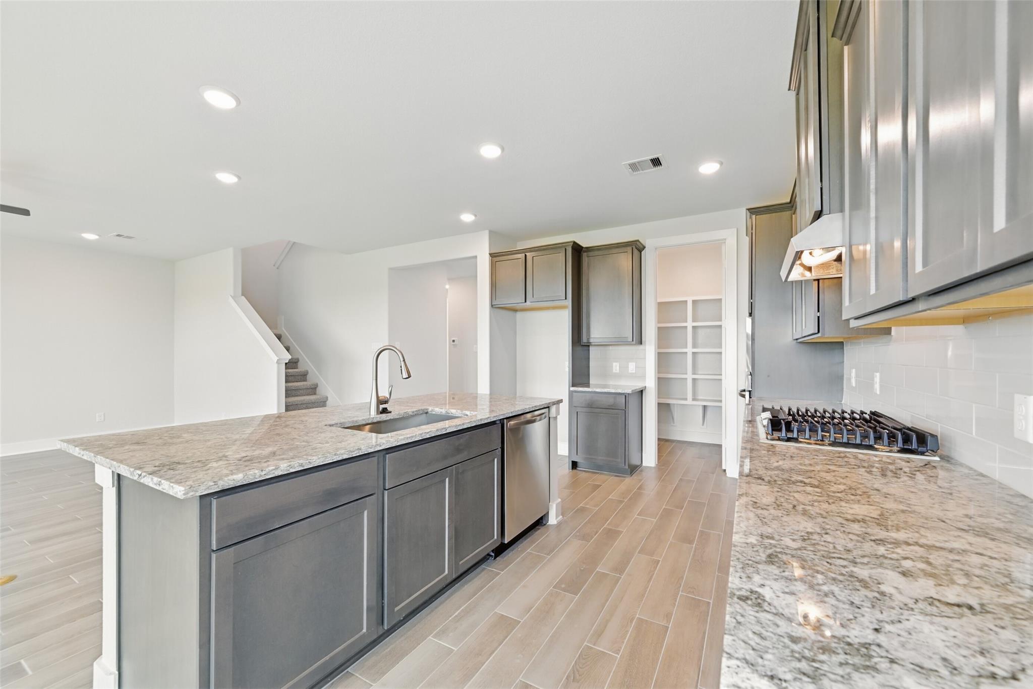 Modern open-concept kitchen with granite island, gray shaker cabinets, stainless appliances in The Philip A home, Lago Mar, Texas City