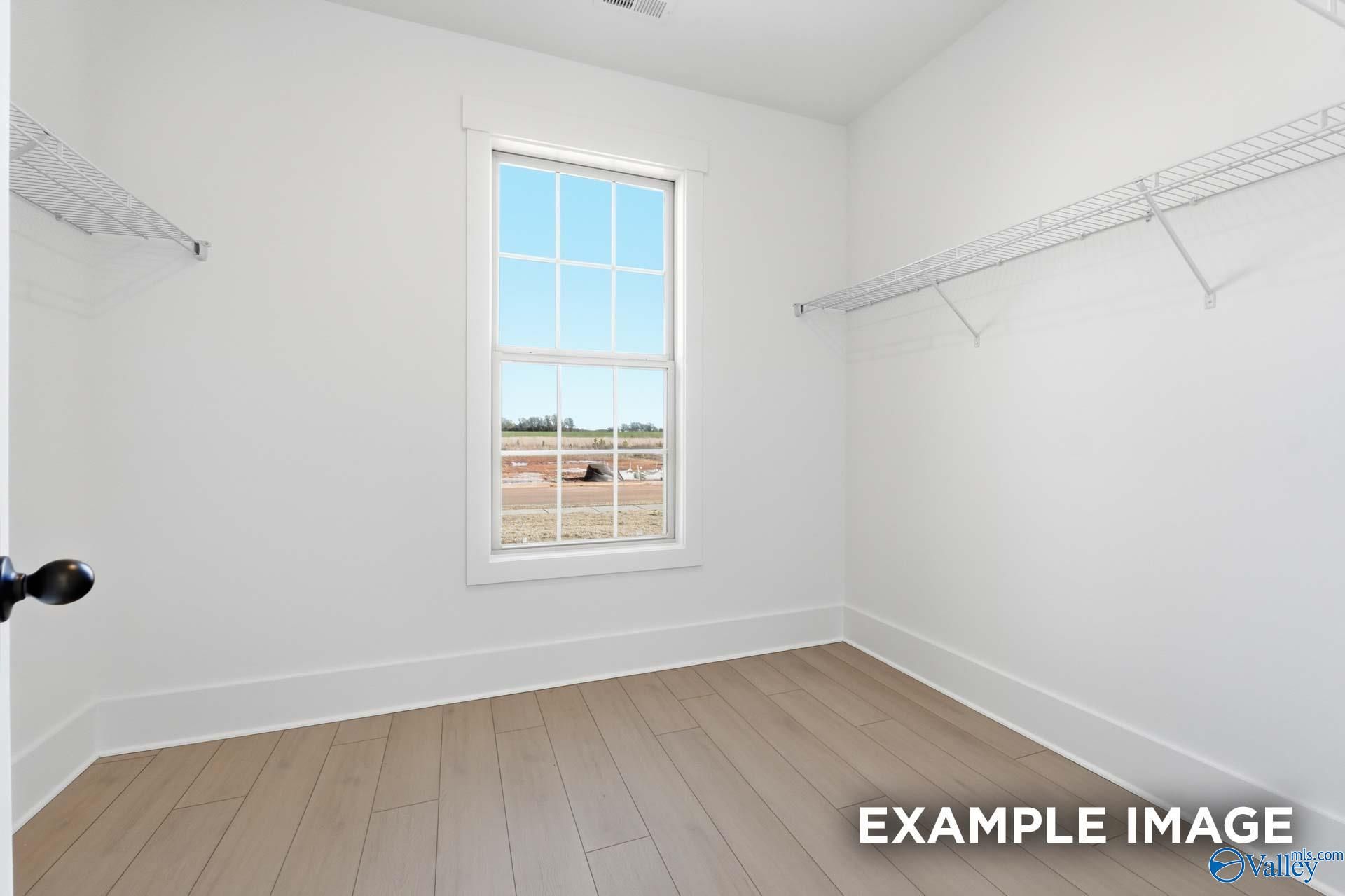 Spacious walk-in closet with built-in shelves, hanging rods, large window, and hardwood floors in Davidson Homes The Emory, Decatur, AL