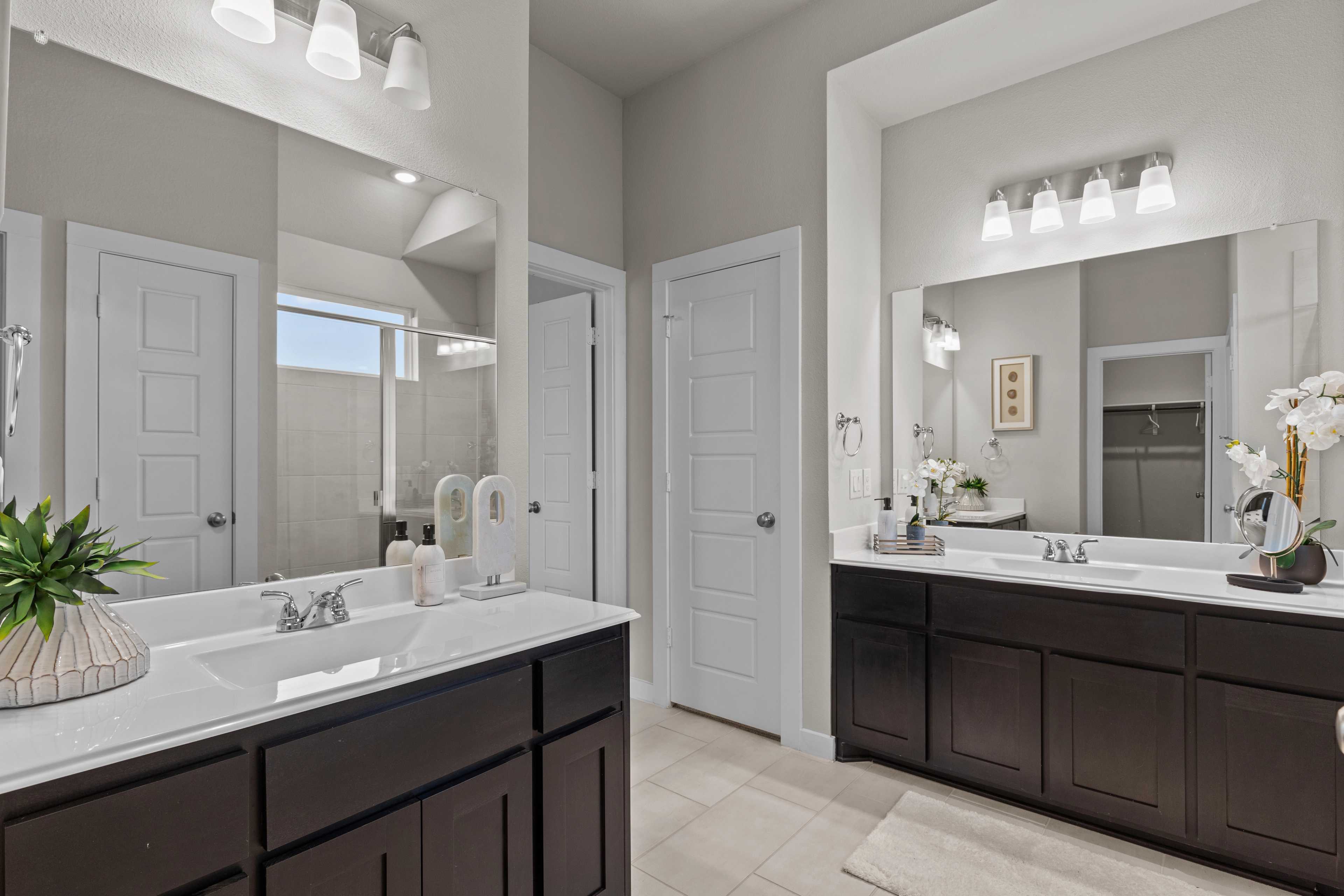 Modern primary bathroom at Hannah Heights in Seguin Texas with double dark wood vanity, large mirrors, and neutral tones