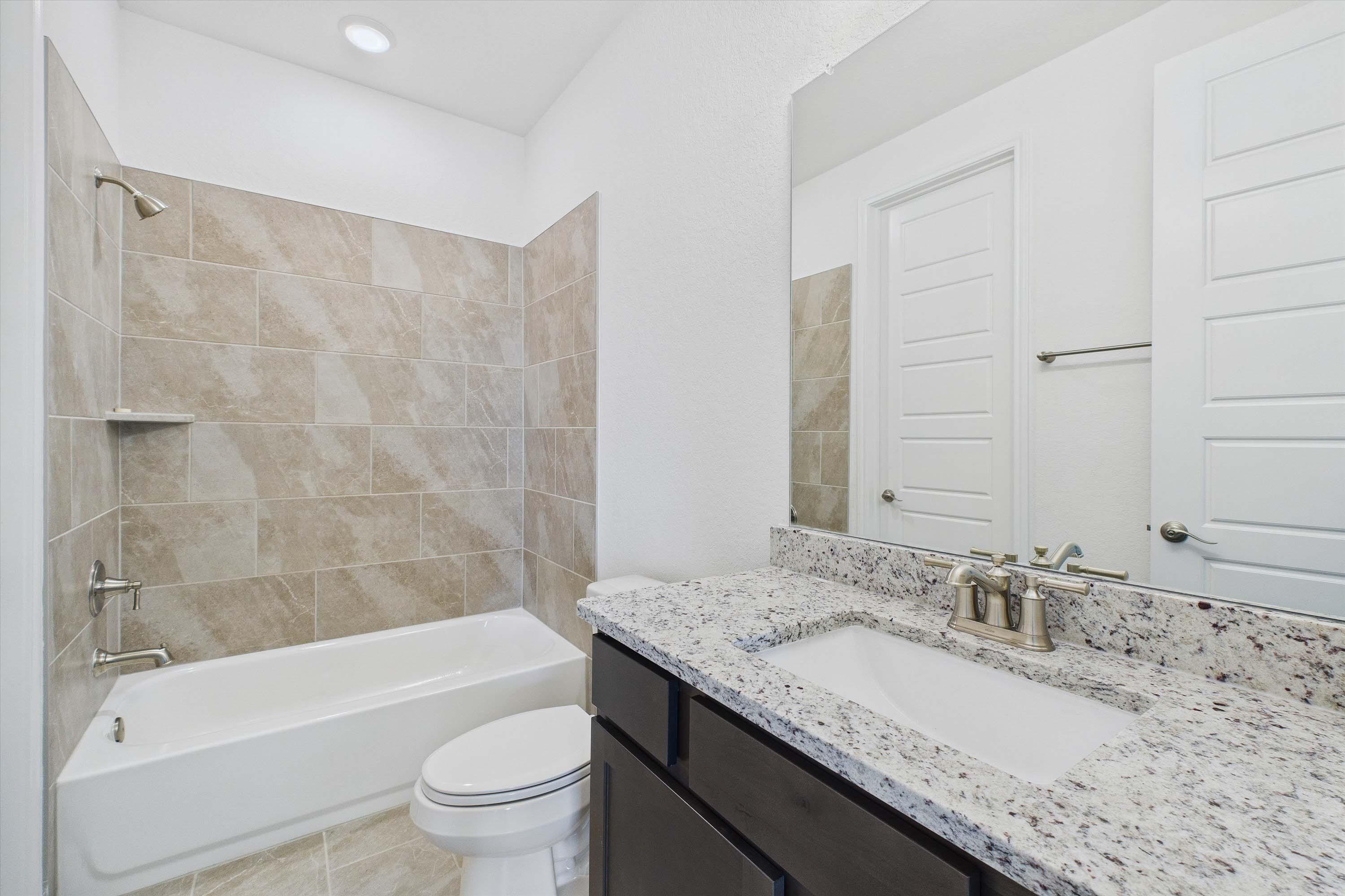 Modern secondary bathroom in The Danbury featuring a granite vanity, dark cabinets, and a tiled tub-shower combination.
