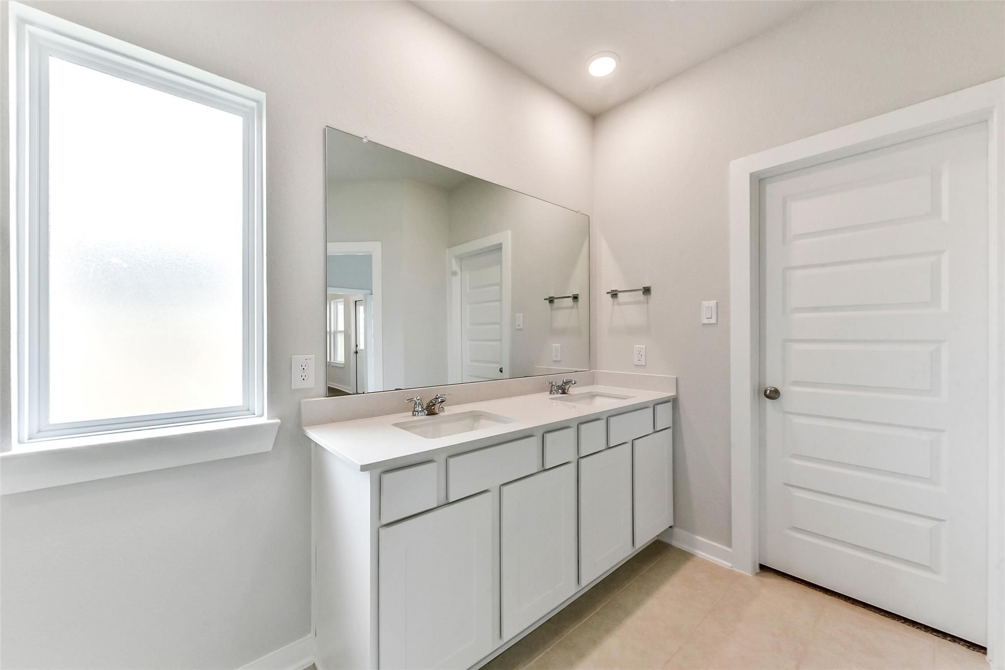 Modern master bathroom with double vanity, large frameless mirror, and window in Davidson Homes The Costa B, Dayton, Texas