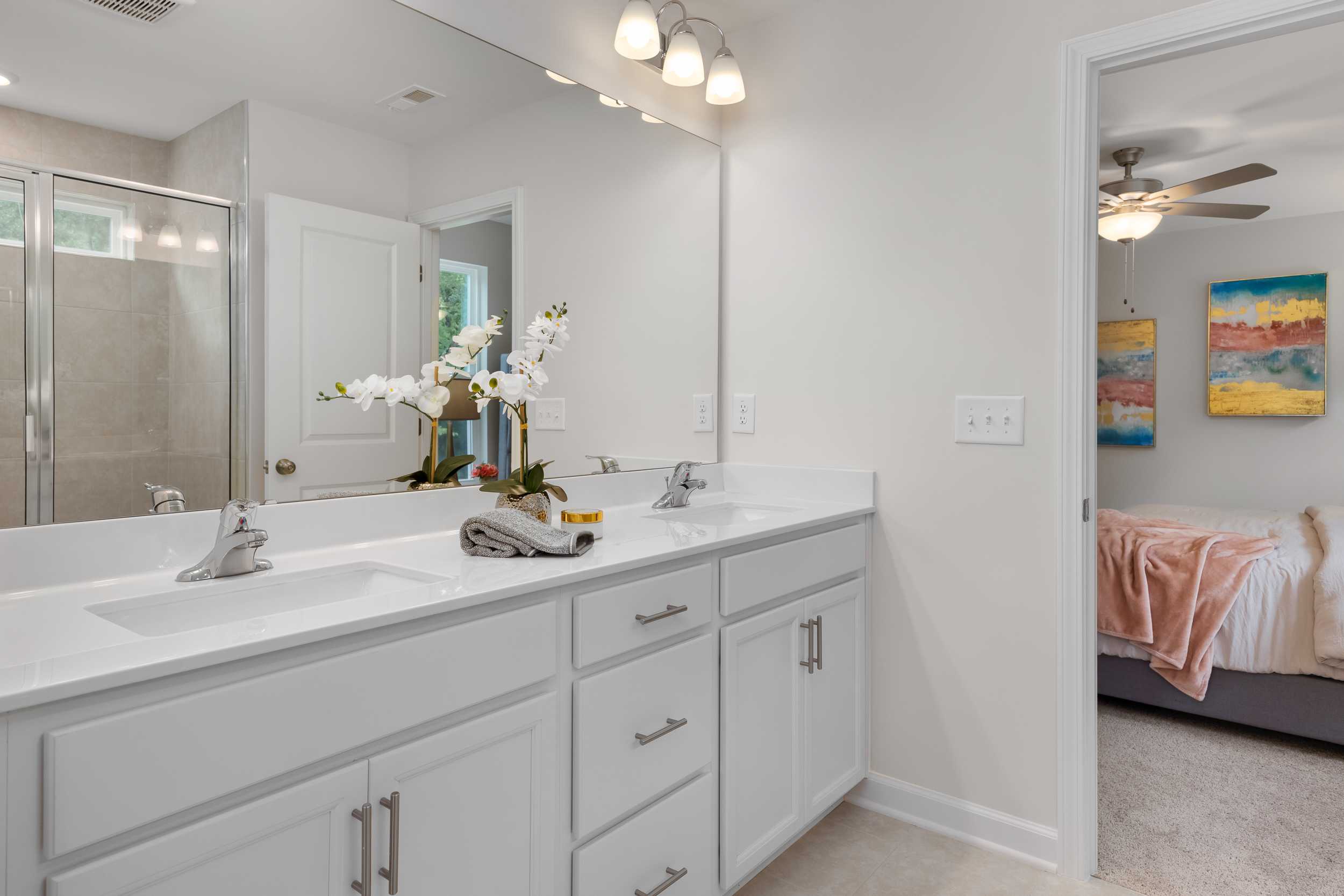 Spacious master bathroom at Gregory Village in Lillington NC featuring white double vanity, orchids, and bedroom view
