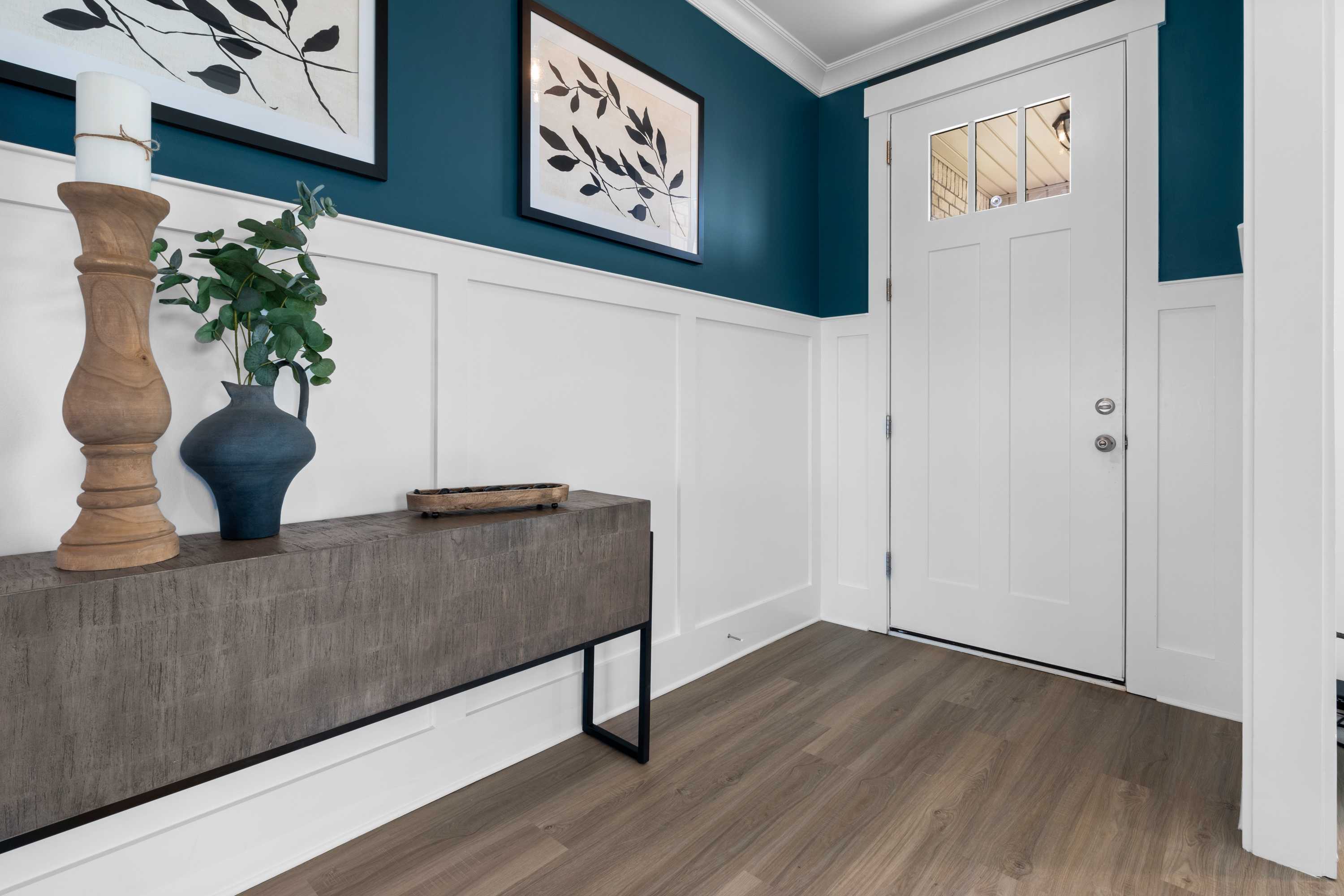 Stylish foyer in The Chelsea B home with teal accent wall, leaf artwork, wooden console table, and white paneled door