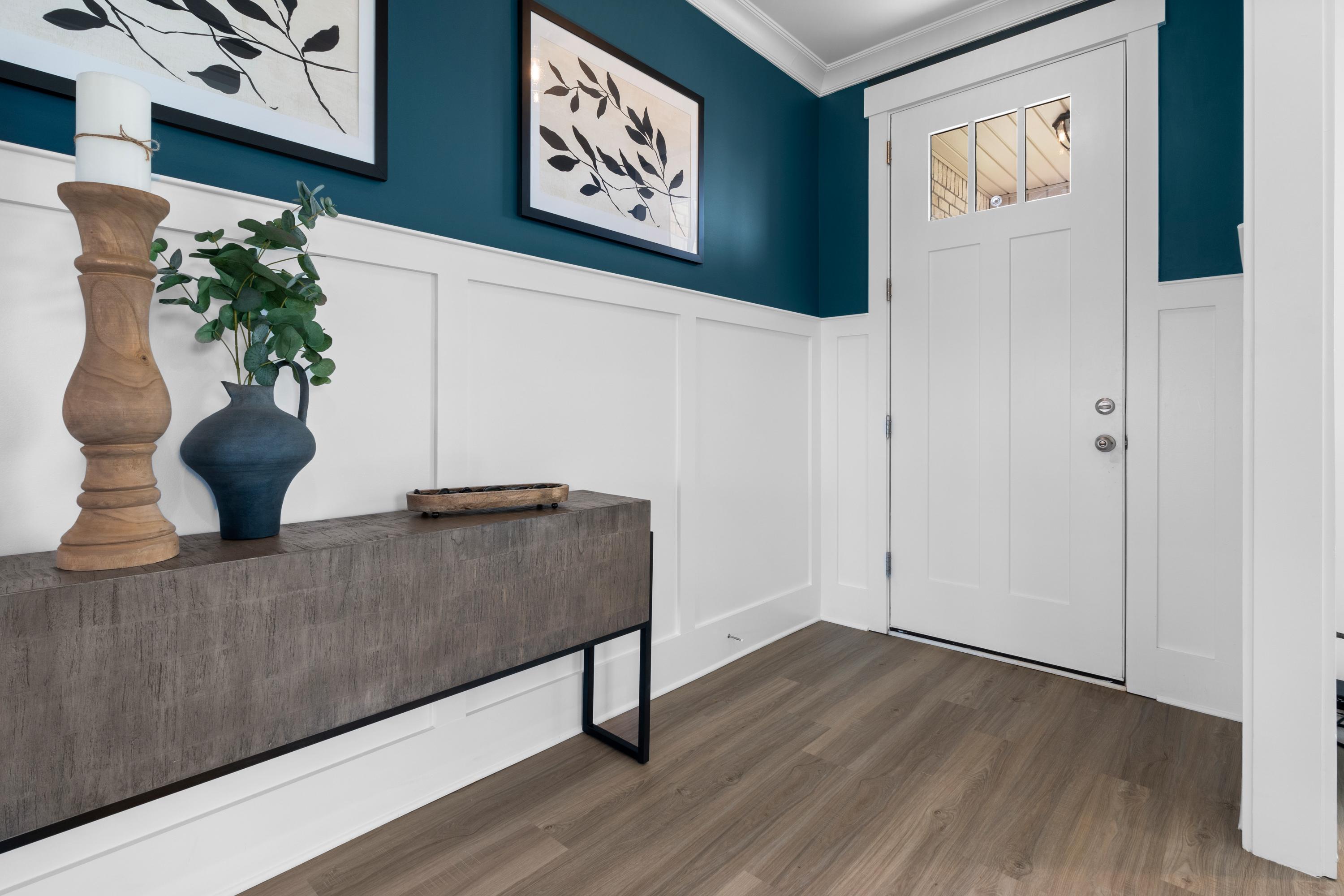 Stylish entryway in The Chelsea A home with teal accent wall, botanical art, wooden console table, and white paneled door