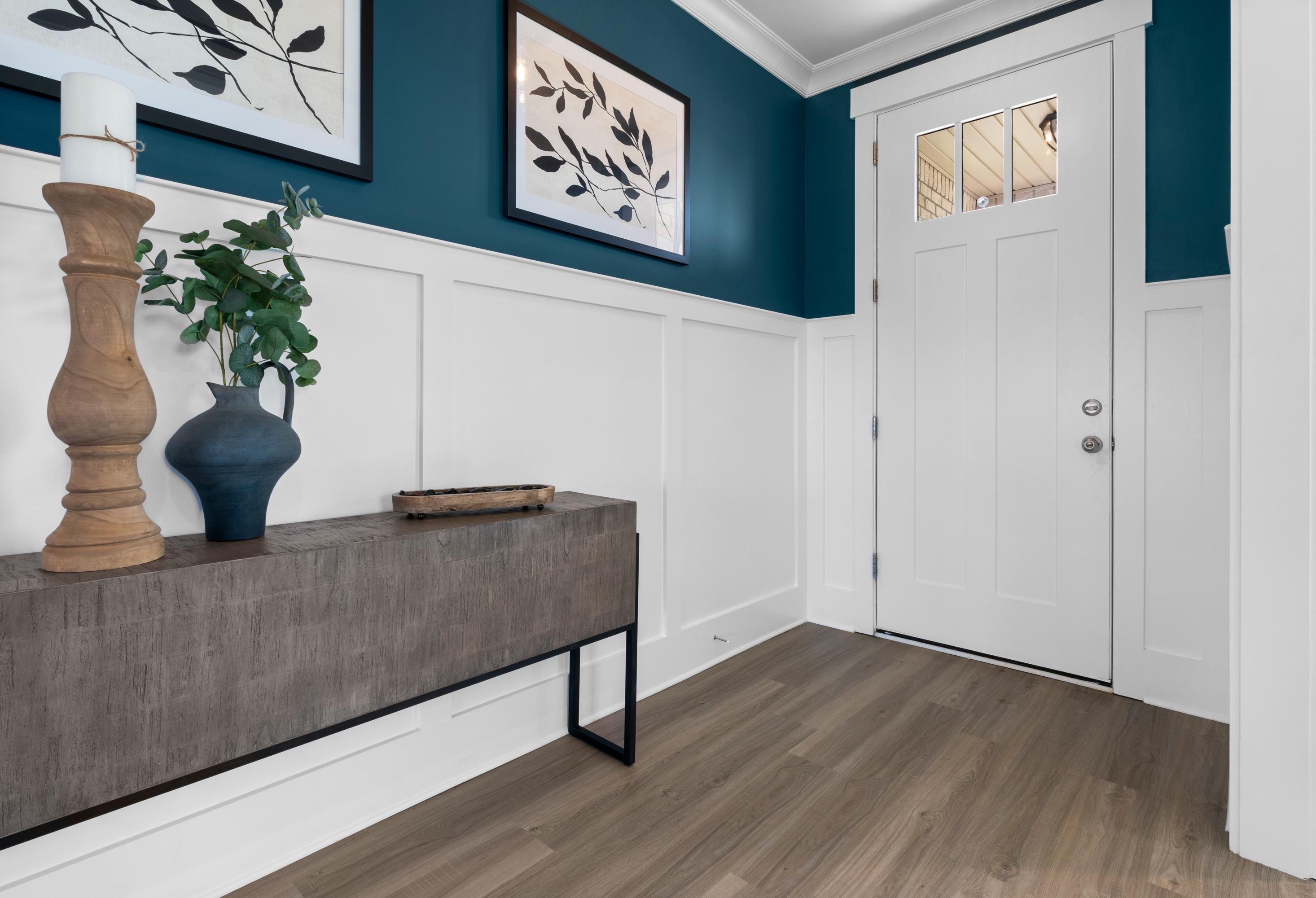Stylish entryway in The Chelsea A home with teal accent wall, botanical art, wooden console table, and white paneled door