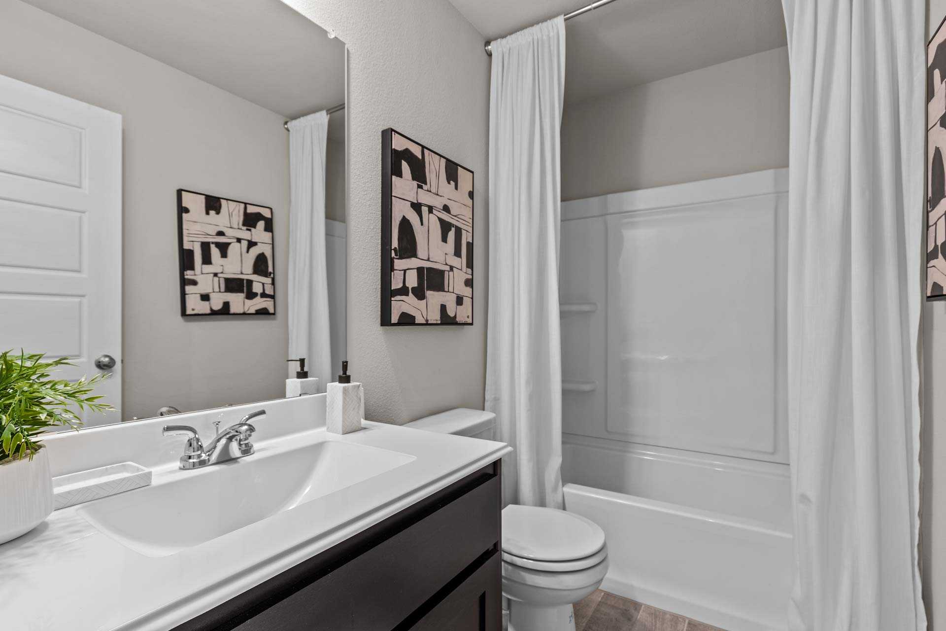 Spacious master bathroom in The Collin B with white tub, dual-sink vanity, toilet, and abstract wall art
