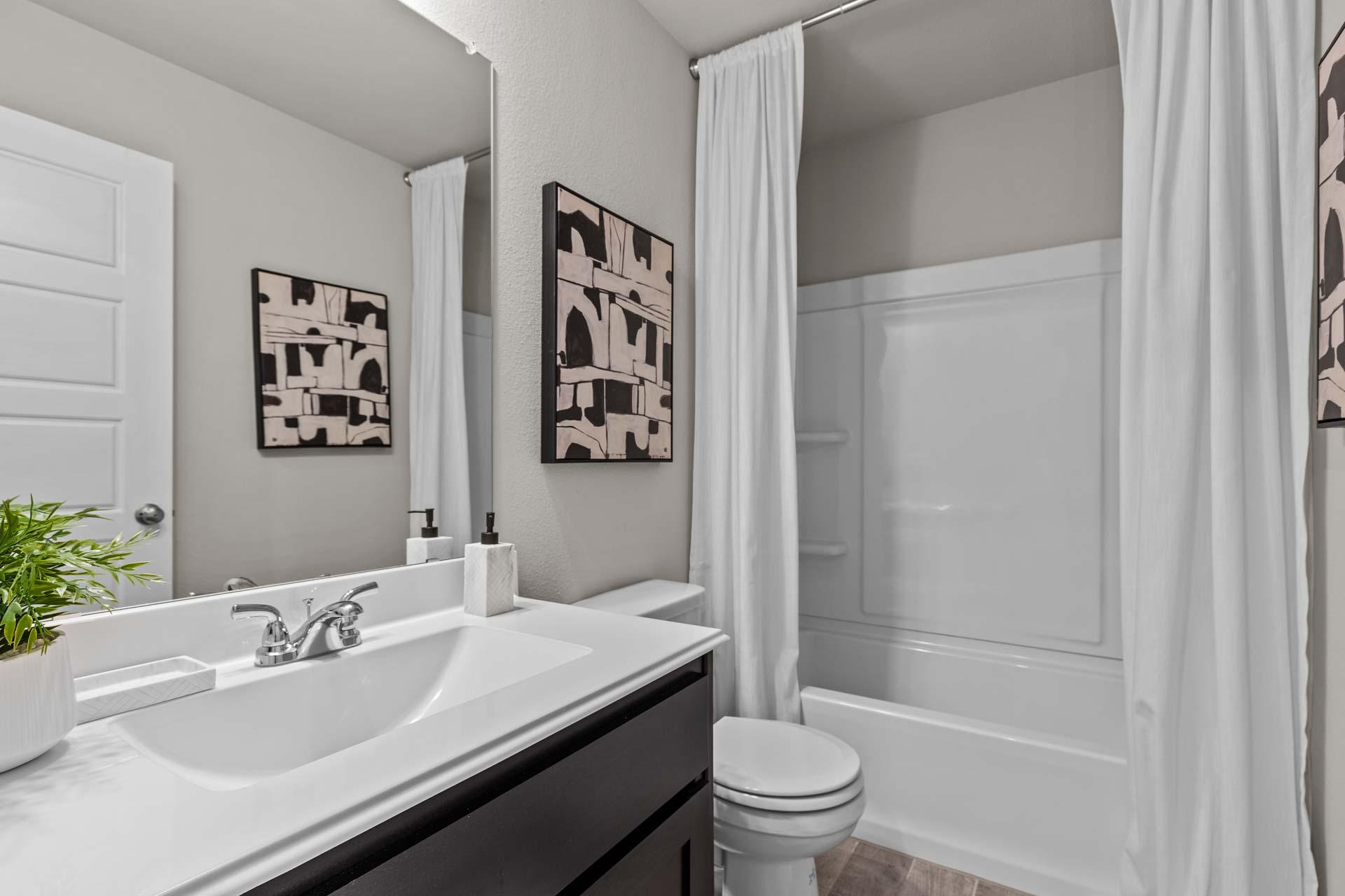 Spacious master bathroom in The Collin A with white tub-shower combo, dark vanity sink, and abstract art accents