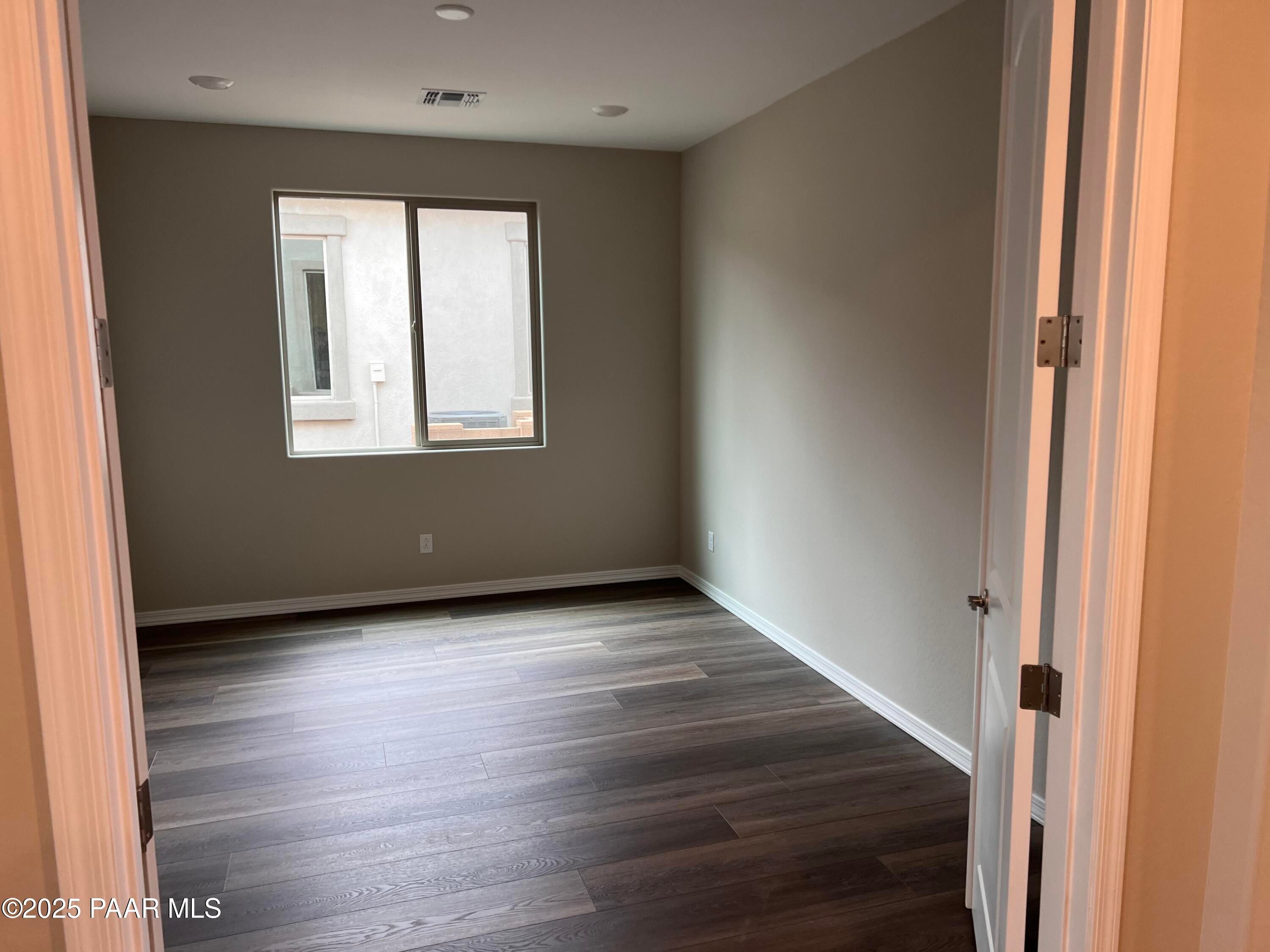 Spacious empty bedroom with beige walls, large window, and laminate wood flooring in Davidson Homes The Harmony A, Prescott Valley, AZ