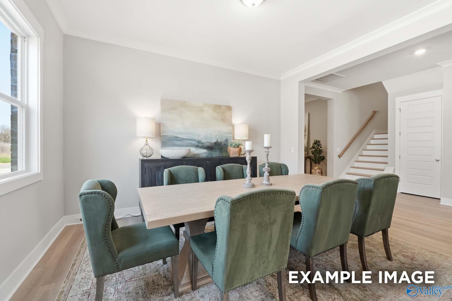 Elegant dining room with rectangular wood table, green velvet chairs, abstract wall art, and open staircase in The Oxford B by Evermore Homes, Owens Cross Roads, Alabama