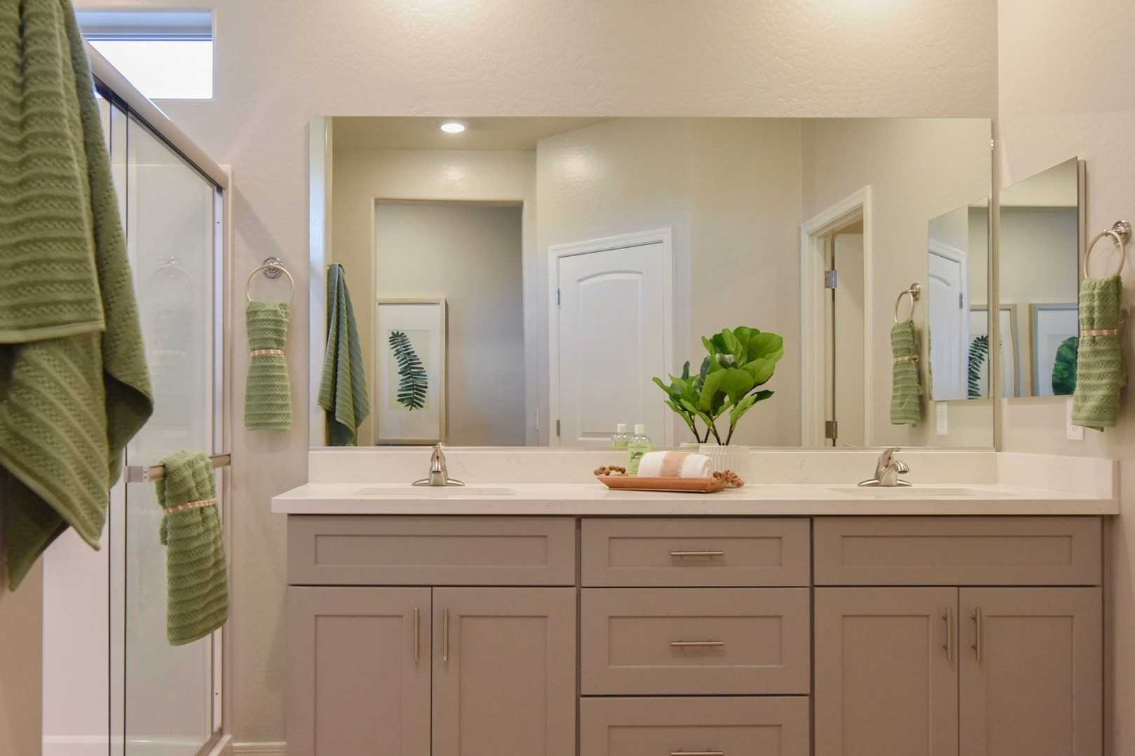 Spacious master bathroom in The Harmony with double vanity, large mirrors, glass shower, and green accents