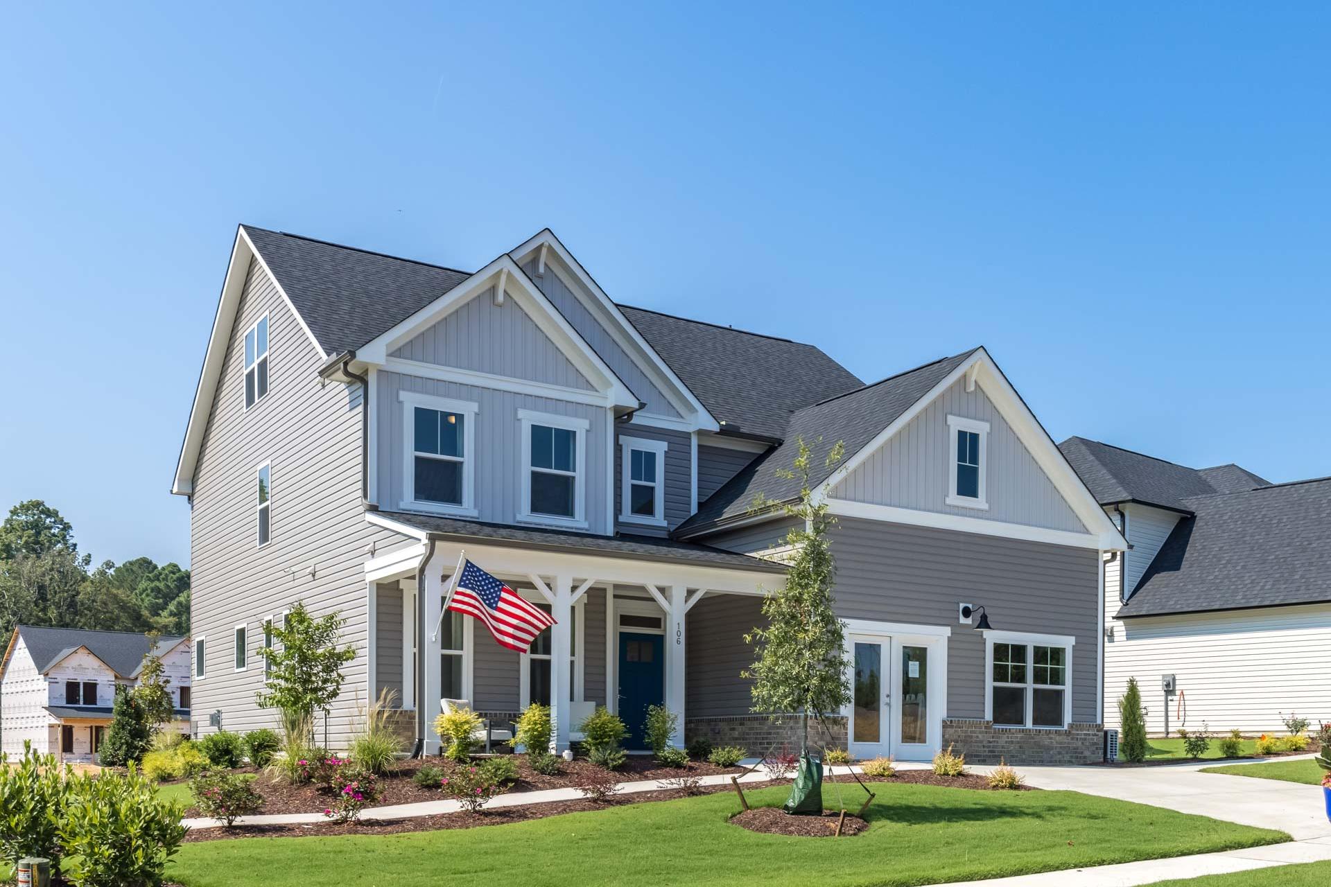 Two-story Craftsman home exterior in Highland Forest, Fuquay-Varina NC with covered front porch, American flag, and lush landscaping