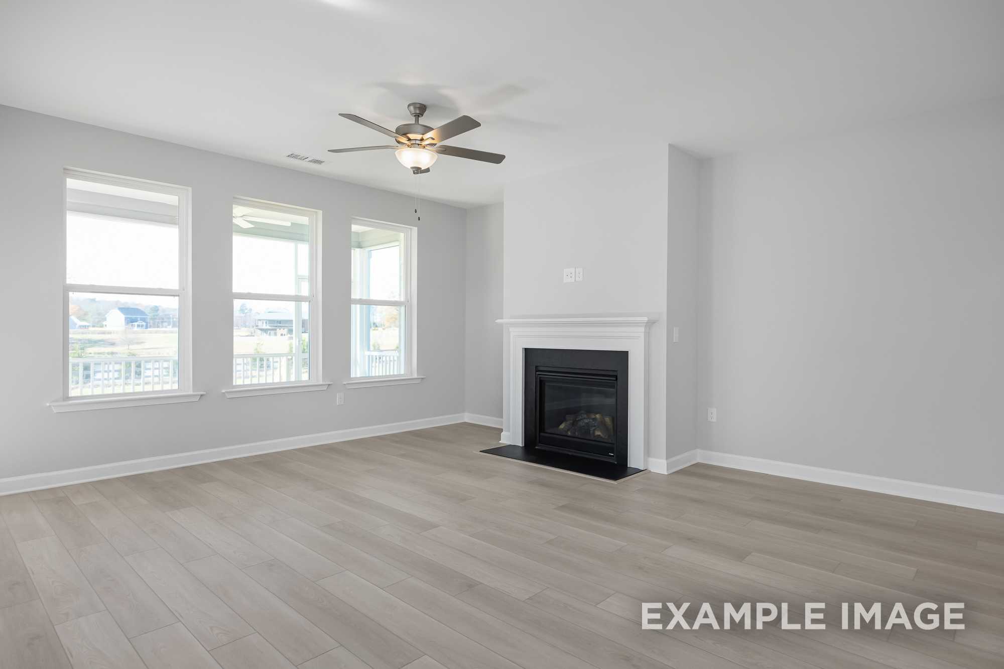 Spacious living room in The Cypress D II with modern gas fireplace, ceiling fan, hardwood floors, and large windows