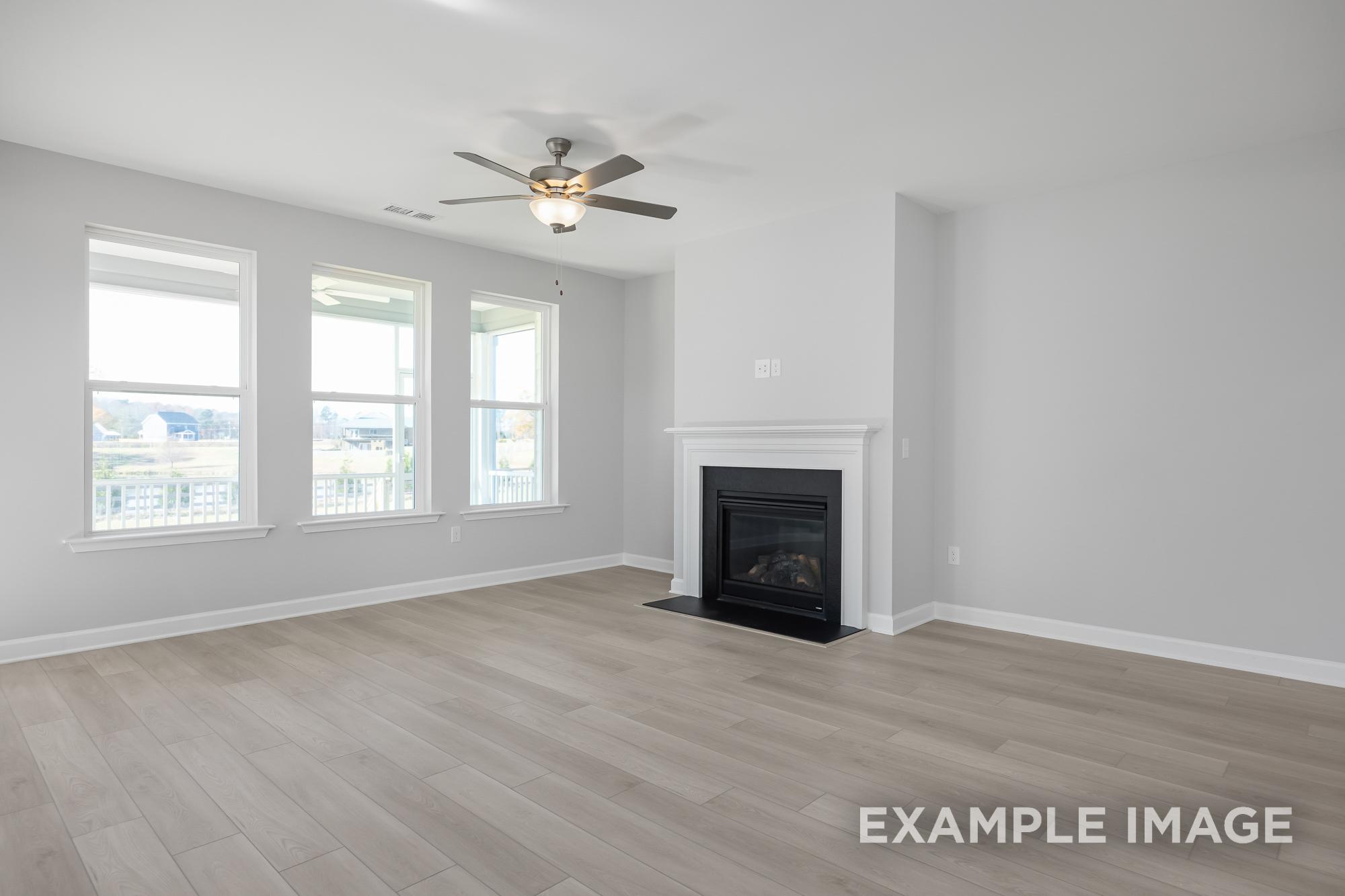 Spacious living room in The Cypress B II with gas fireplace, ceiling fan, hardwood floors, and large windows
