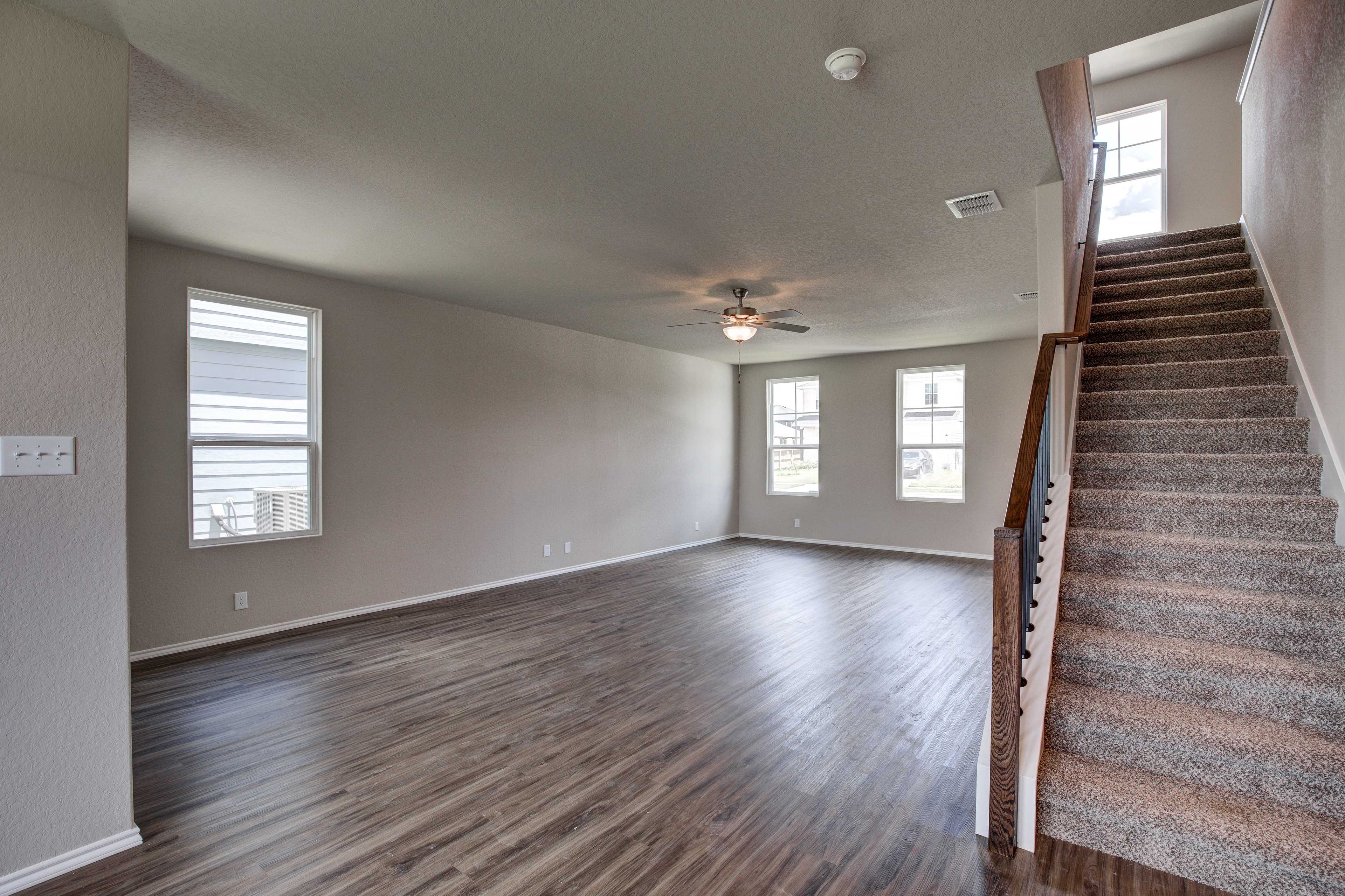 Spacious open-concept living area in The Murray 2-story home with hardwood floors, large windows, ceiling fan, and carpeted staircase
