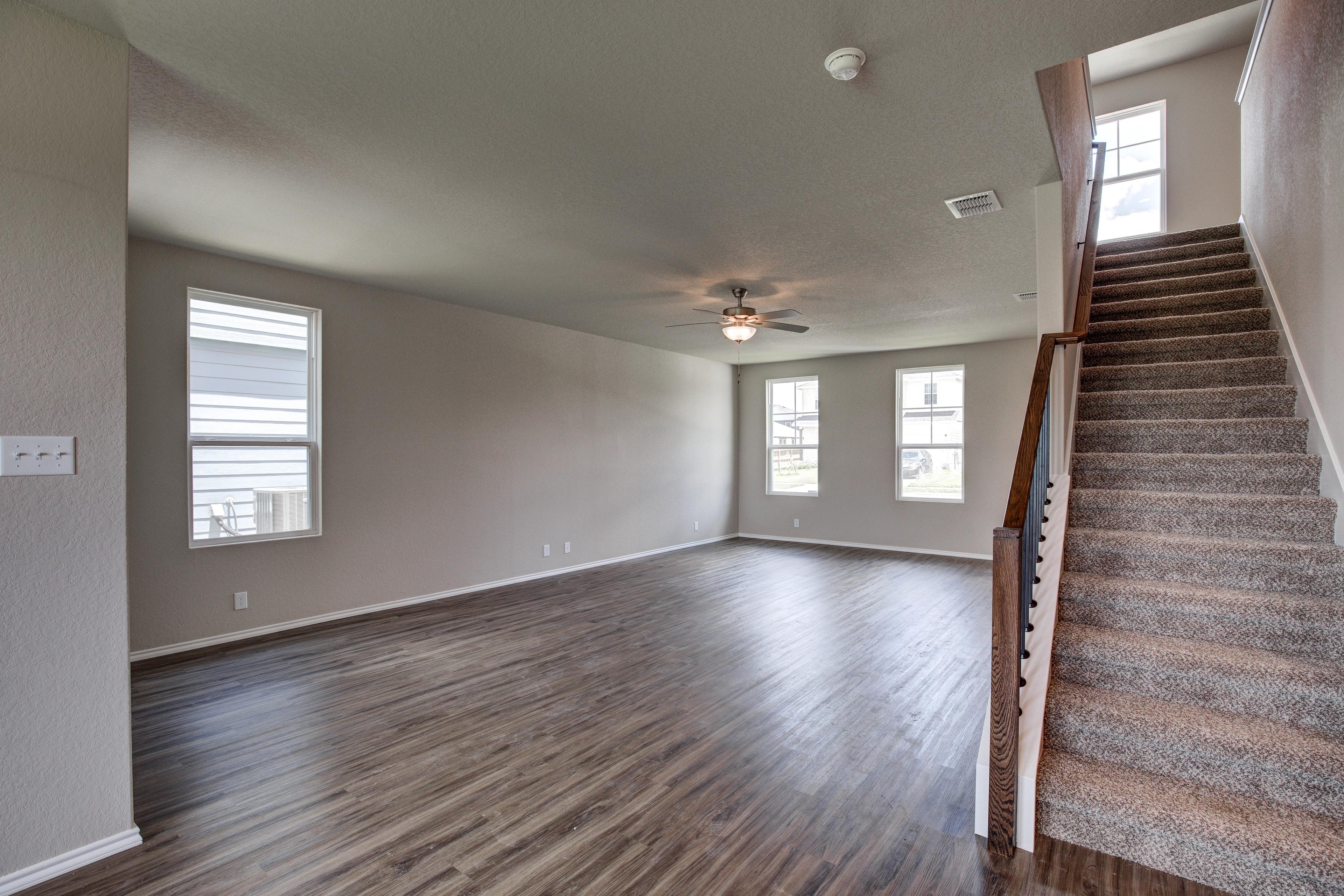 Spacious open living room in The Murray G with light wood floors, large windows, ceiling fan, and carpeted wooden staircase