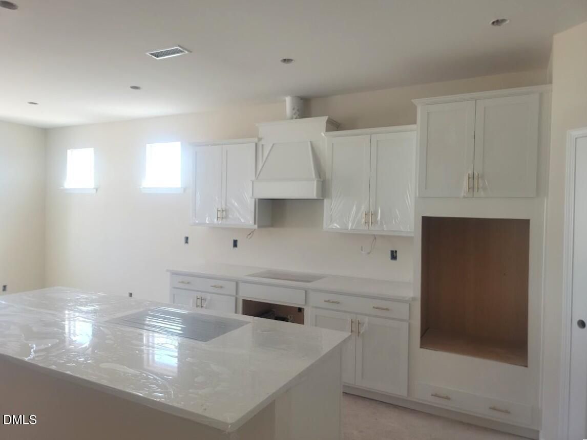 Modern white shaker kitchen with large island, stainless hood, and ample cabinets in Davidson Homes The Cypress B II, Angier, NC