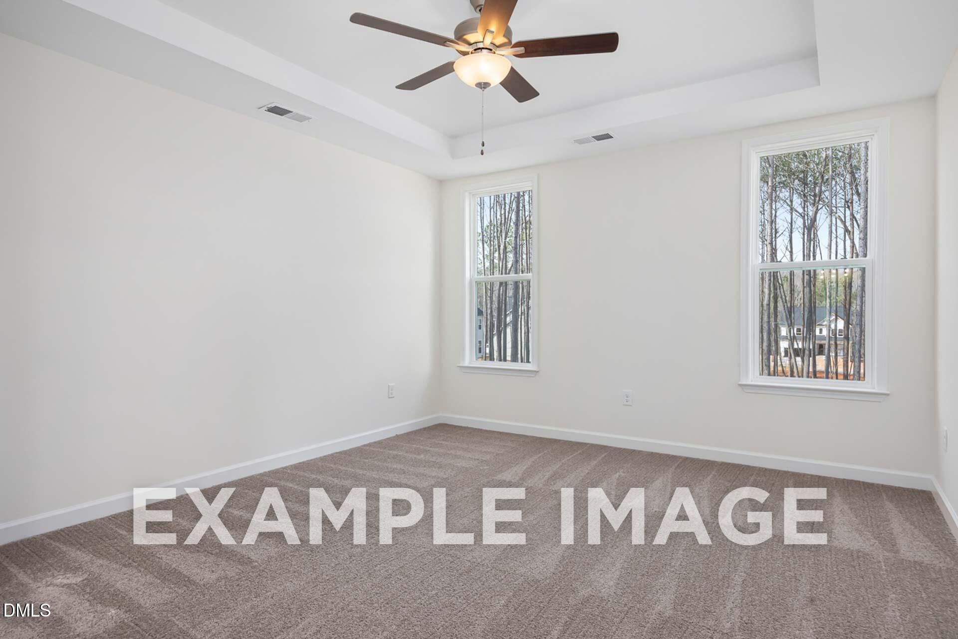 Bright empty bedroom with beige walls, large windows overlooking trees, ceiling fan in The Ash B by Davidson Homes, Zebulon NC