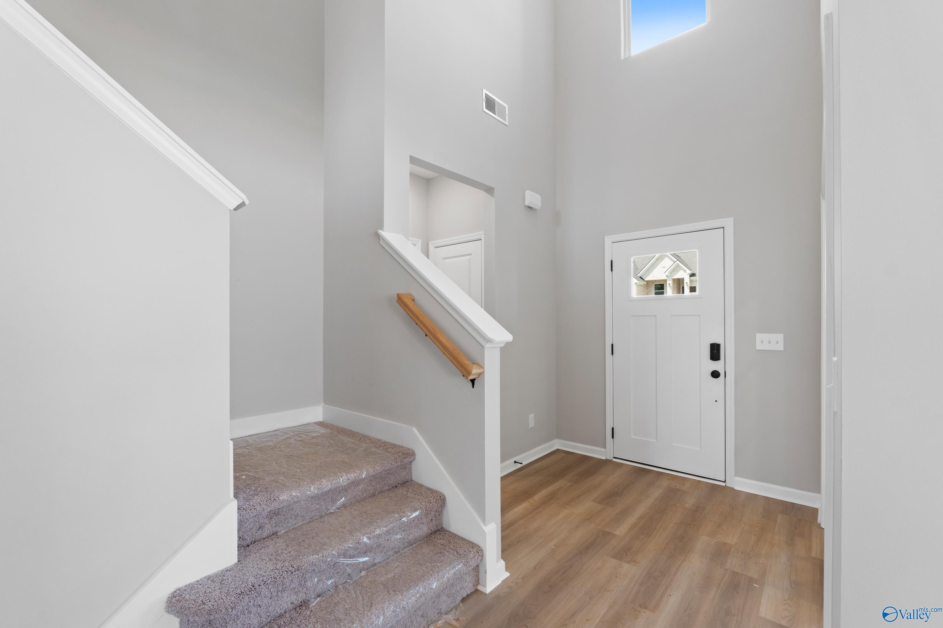 Grand two-story entry foyer with carpeted staircase, high ceilings, and white door in Davidson Homes The Dorado, Huntsville, AL