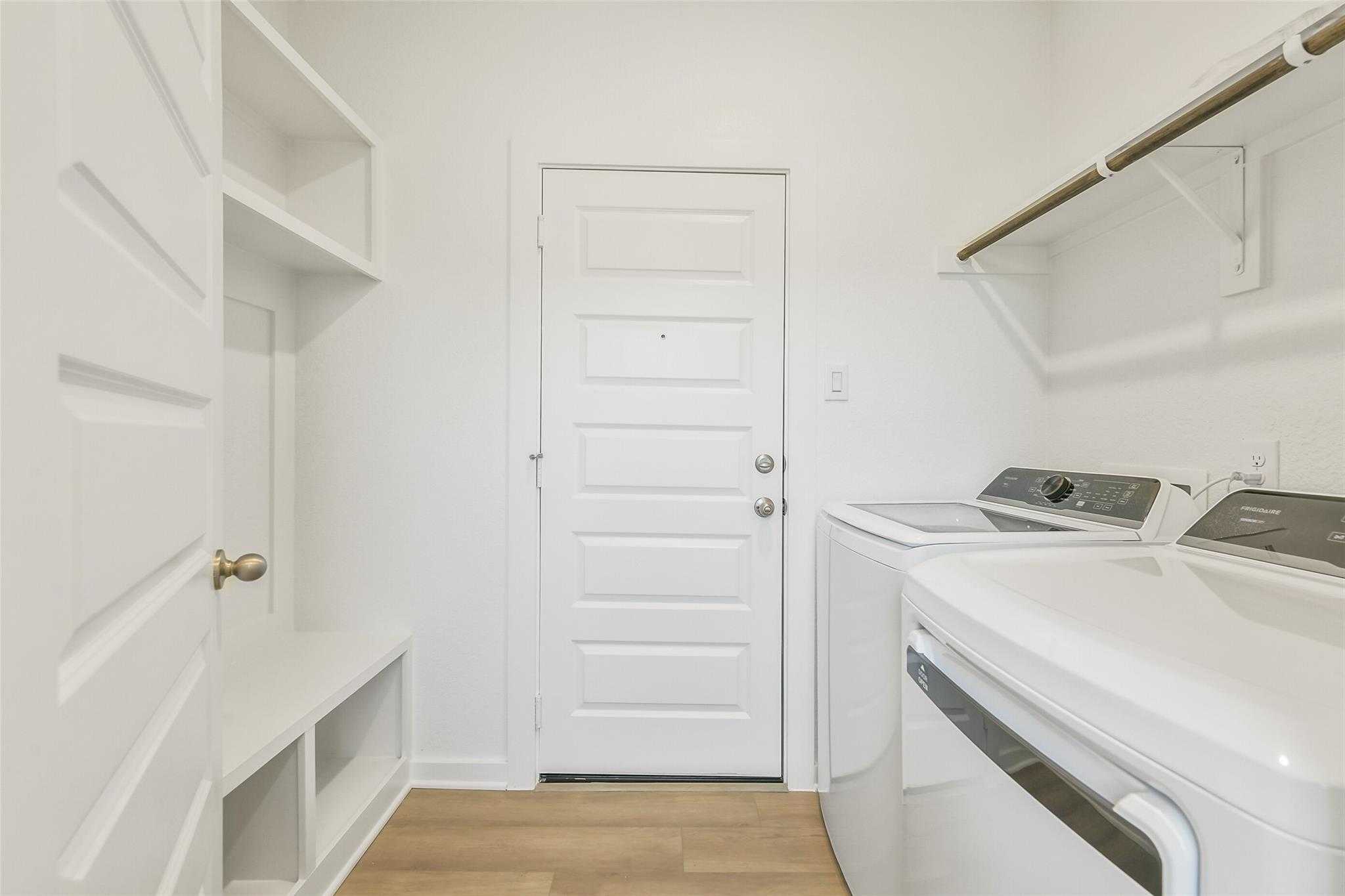 Spacious laundry room with white washer dryer, built-in shelves, bench in 5-bedroom Davidson Homes San Marcos E, Cleveland Texas