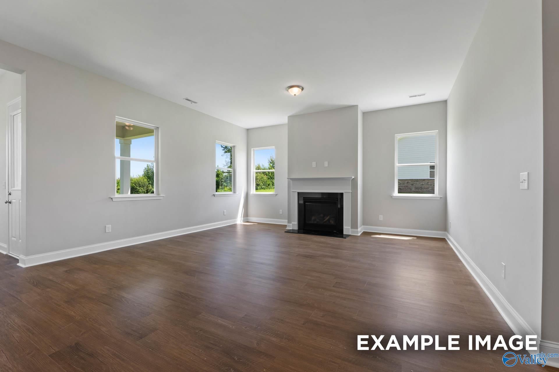 Spacious living room with gas fireplace, hardwood floors, and large windows in Evermore Homes The Arcadia, Owens Cross Roads, Alabama