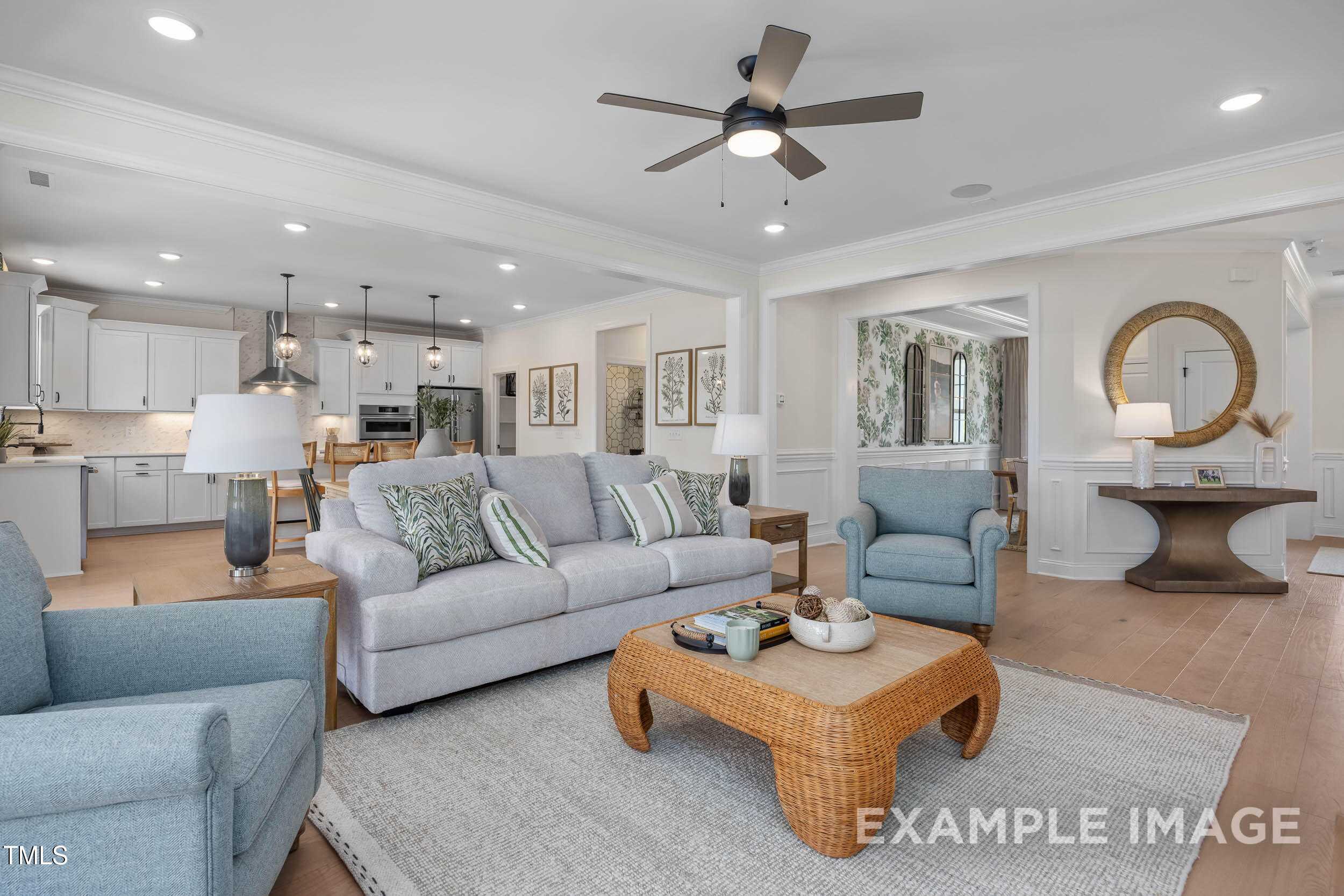 Bright open-concept living room with gray sofa, blue chairs, woven coffee table, and white kitchen in Davidson Homes Crawford B, Raleigh, NC