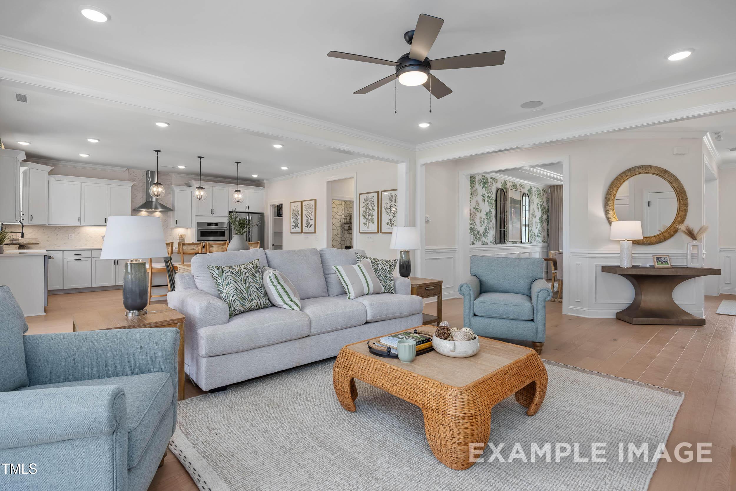 Bright open-concept living room with gray sofa, blue chairs, woven coffee table, and white kitchen in Davidson Homes Crawford B, Raleigh, NC