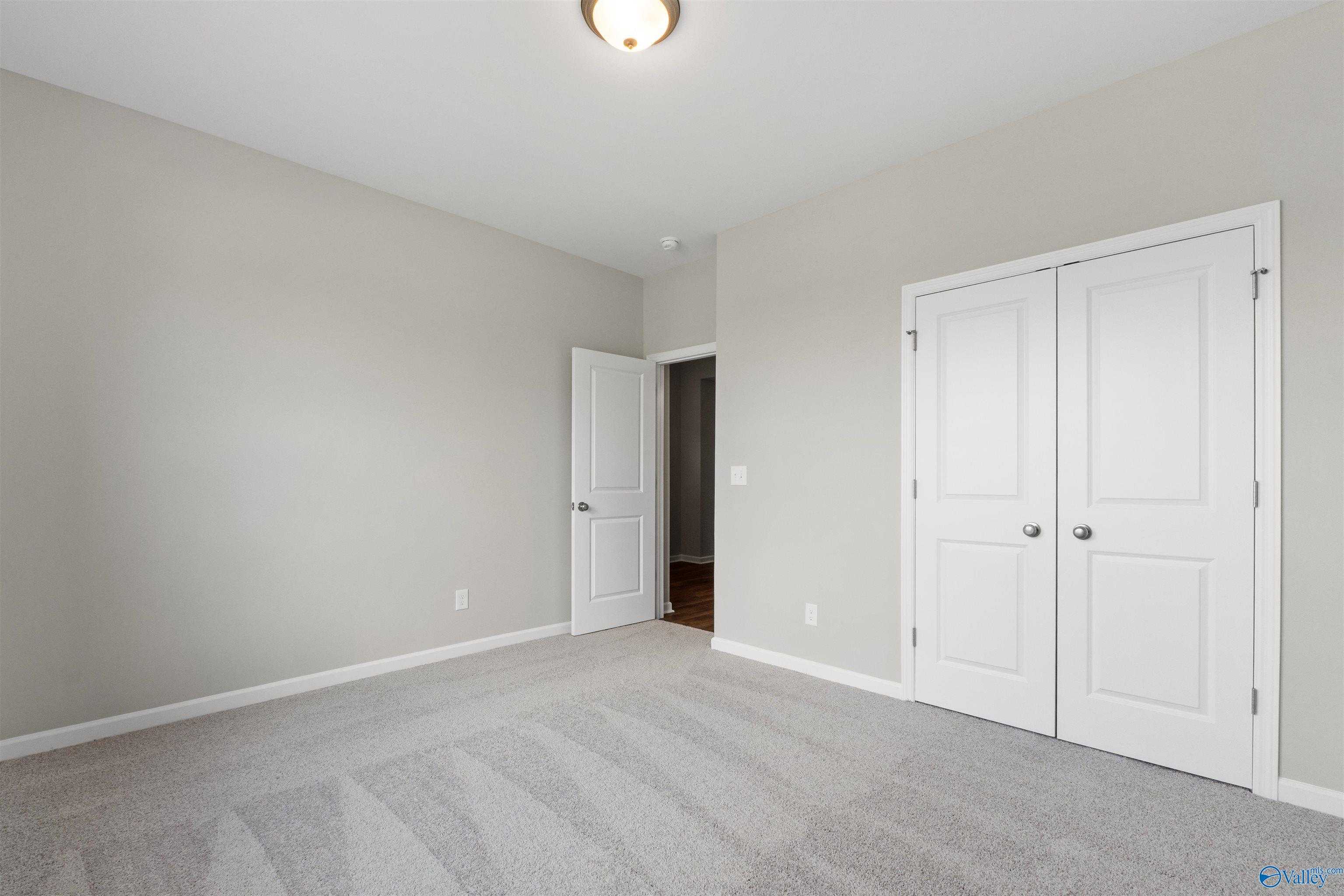 Spacious empty bedroom with light gray walls, white double closet doors, and carpet flooring in Davidson Homes The Luna, Hazel Green, AL