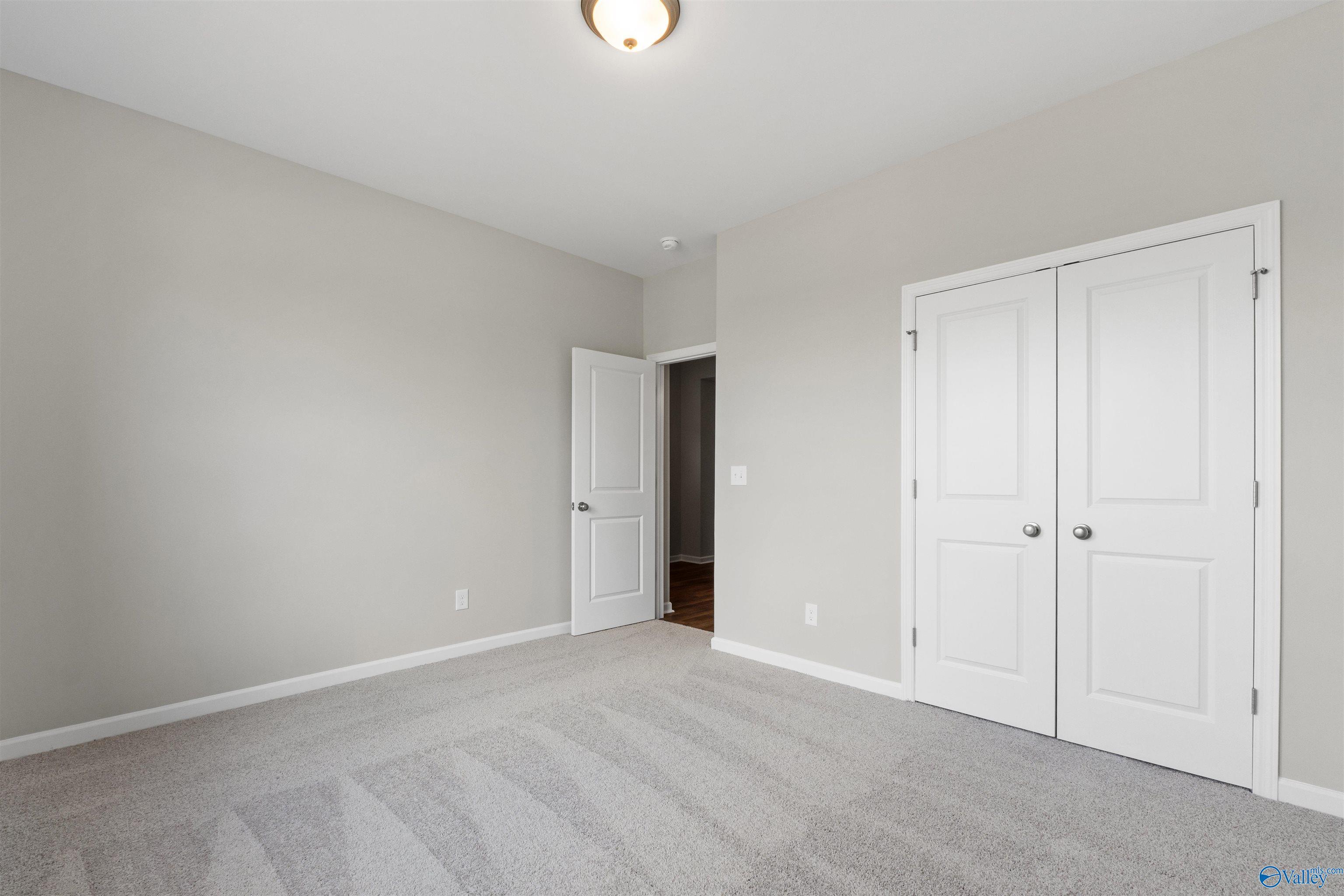 Spacious empty bedroom with light gray walls, white double closet doors, and carpet flooring in Davidson Homes The Luna, Hazel Green, AL