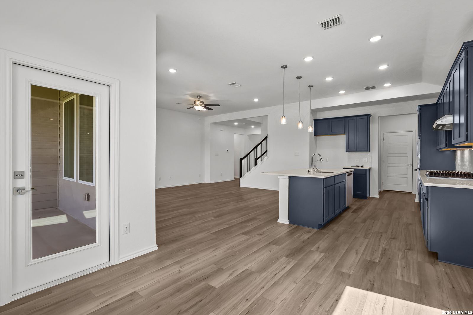 Modern open-concept kitchen with navy cabinets, center island sink, pendant lights, and adjacent living area in Davidson Homes Sequoia B, San Antonio
