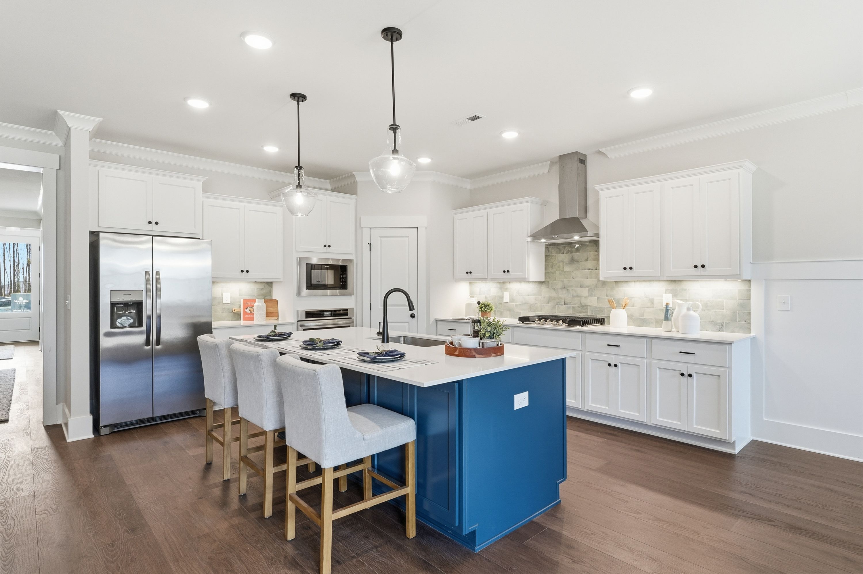 Spacious modern kitchen with white shaker cabinets, blue island, stainless steel appliances, and hardwood floors at Noble Ridge in Cullman Alabama
