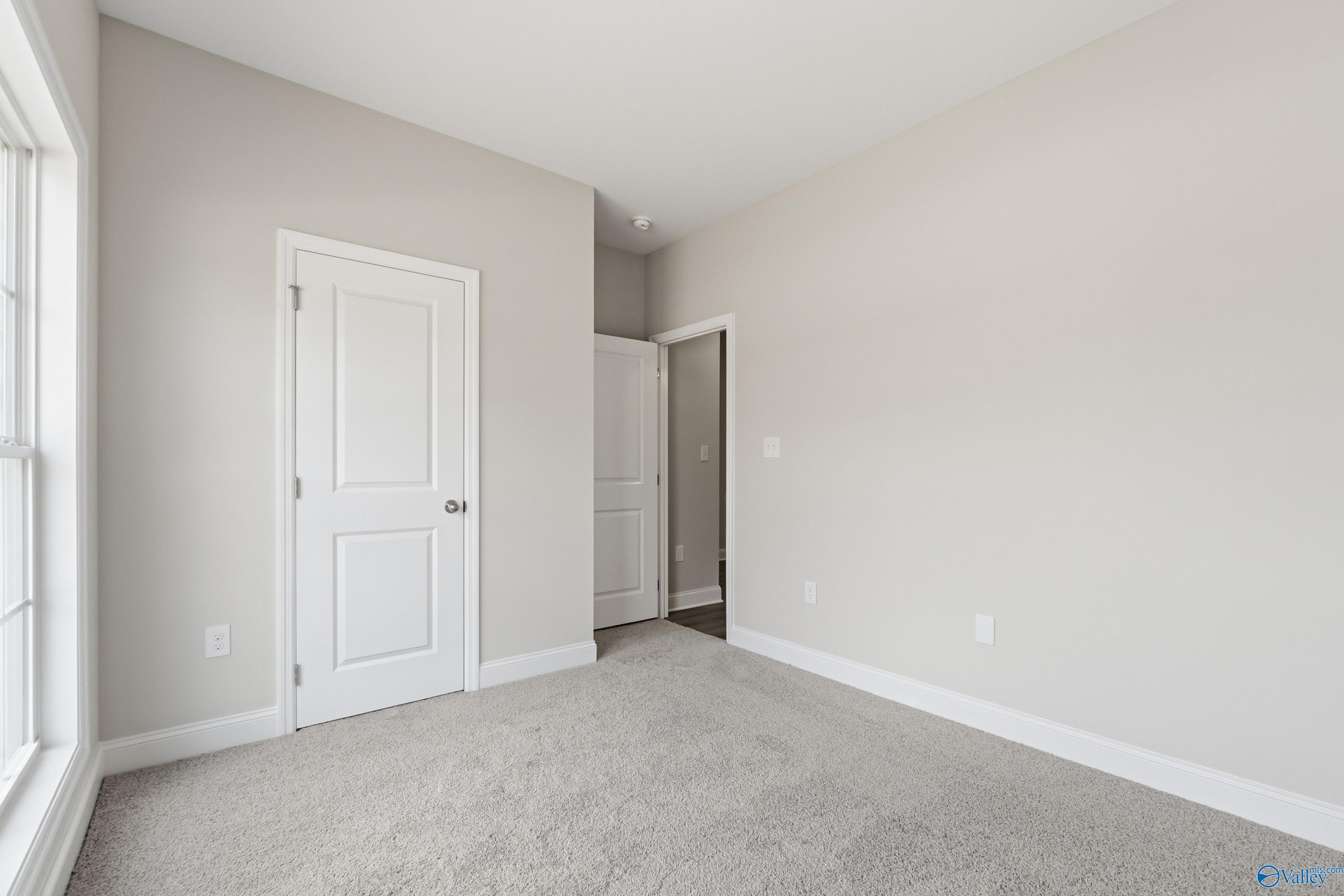 Spacious bedroom with light gray walls, large window, white doors, and carpeted floor in Davidson Homes The Asheville C, Huntsville