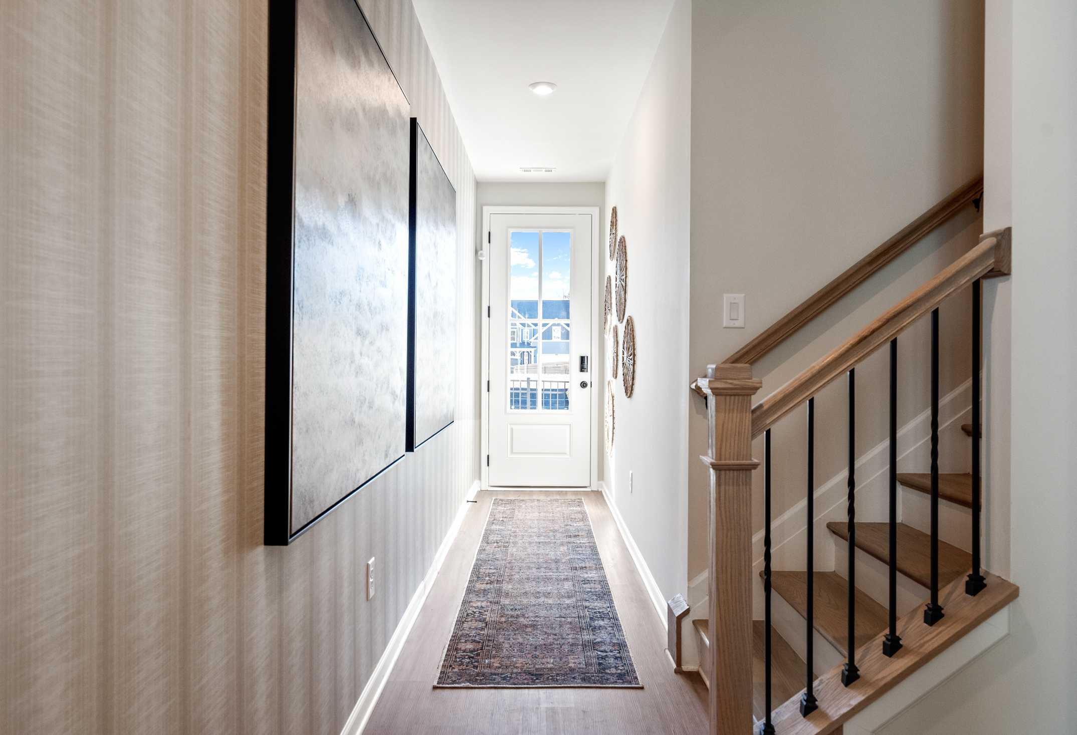 Spacious hallway in The Marion A by Davidson Homes featuring large abstract artwork, runner rug, and oak staircase to upper floor