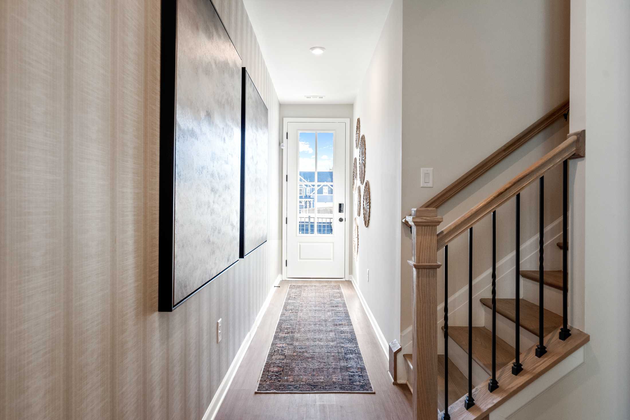 Spacious entry hallway in The Marion B home with abstract wall art, oak staircase, runner rug, and front door