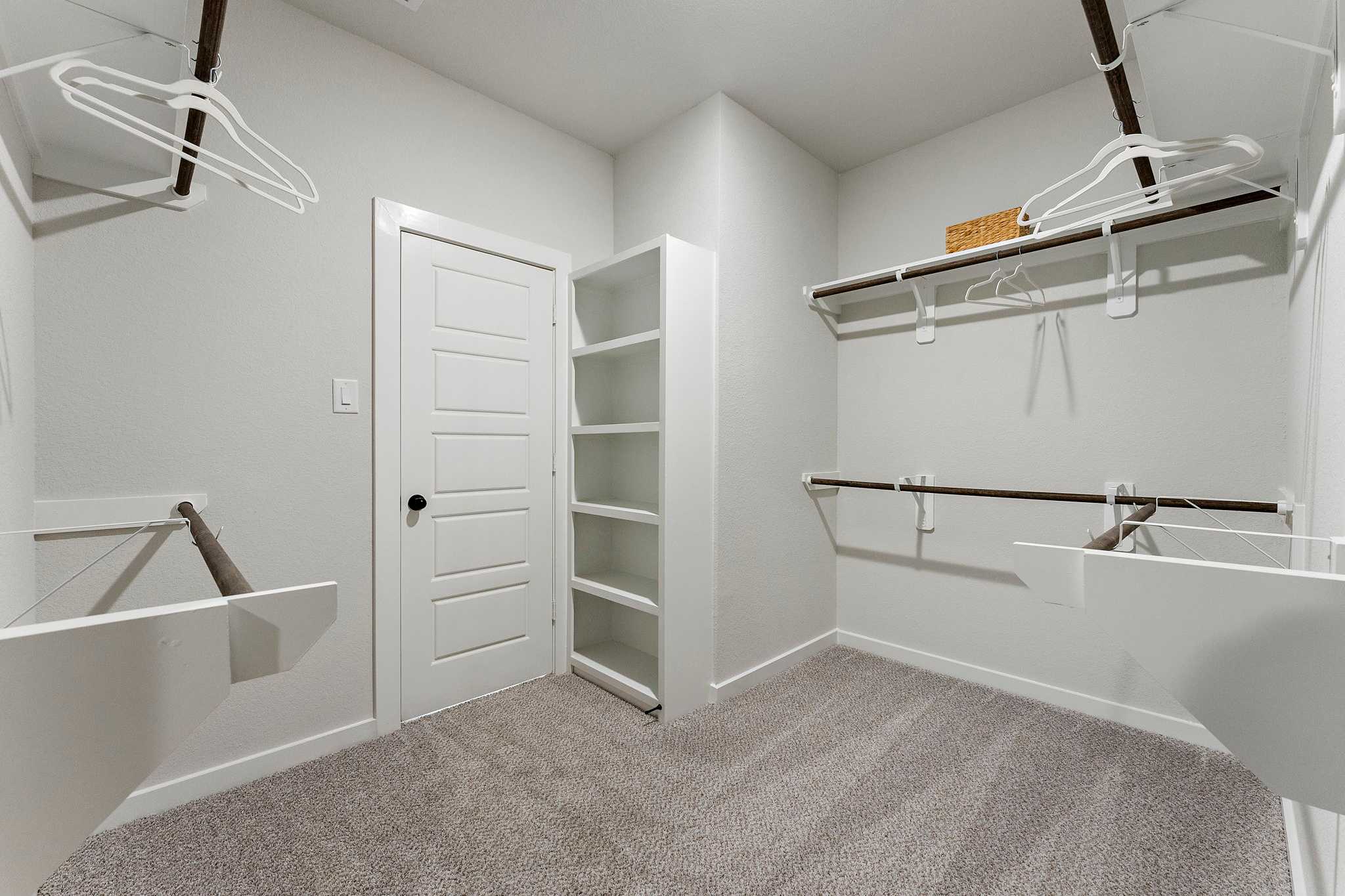 Spacious walk-in closet at Sundance Cove in Crosby Texas by Davidson Homes with built-in shelving, hanging rods and gray carpet